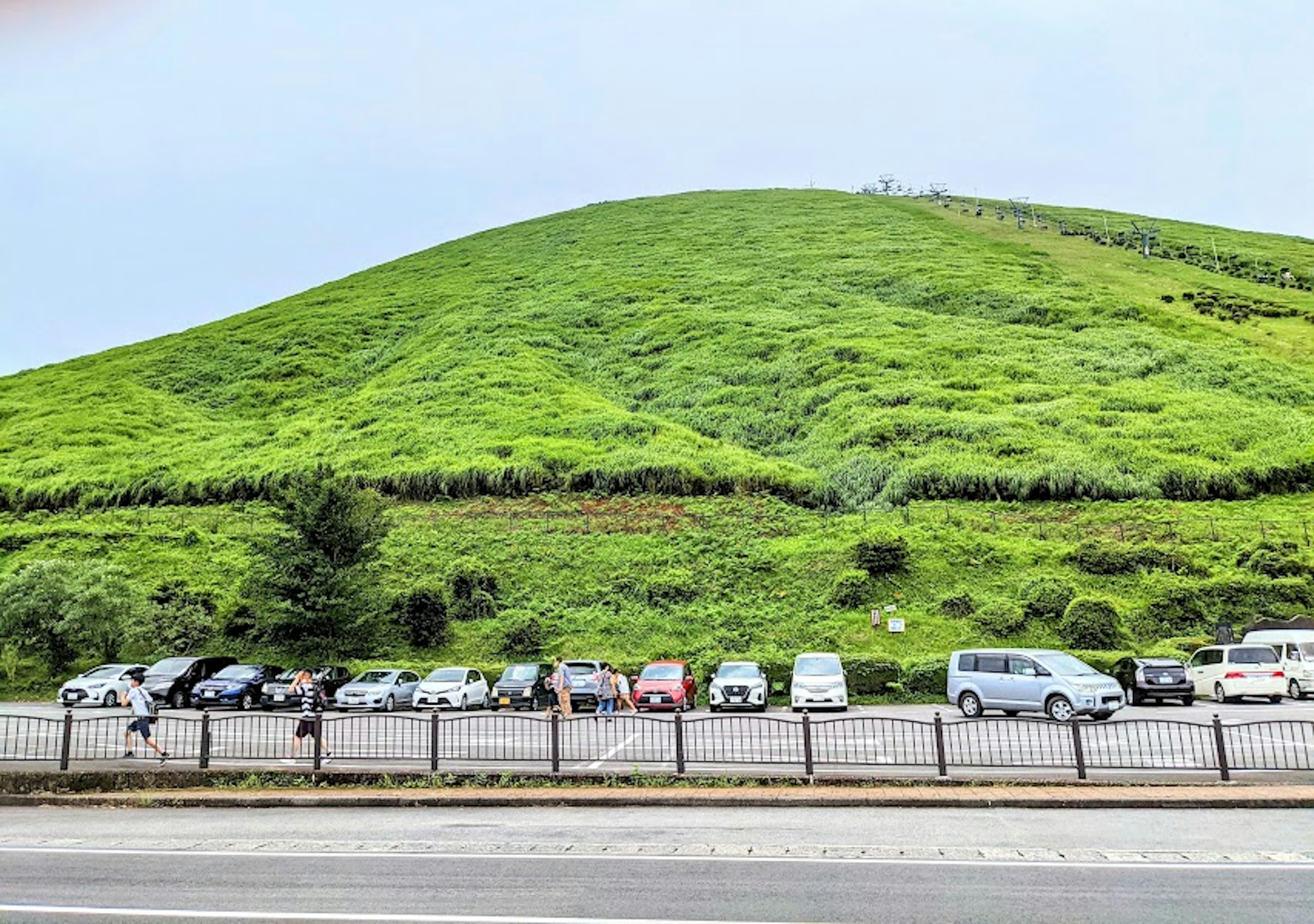 Tempat parkir dengan kendaraan di depan bukit hijau