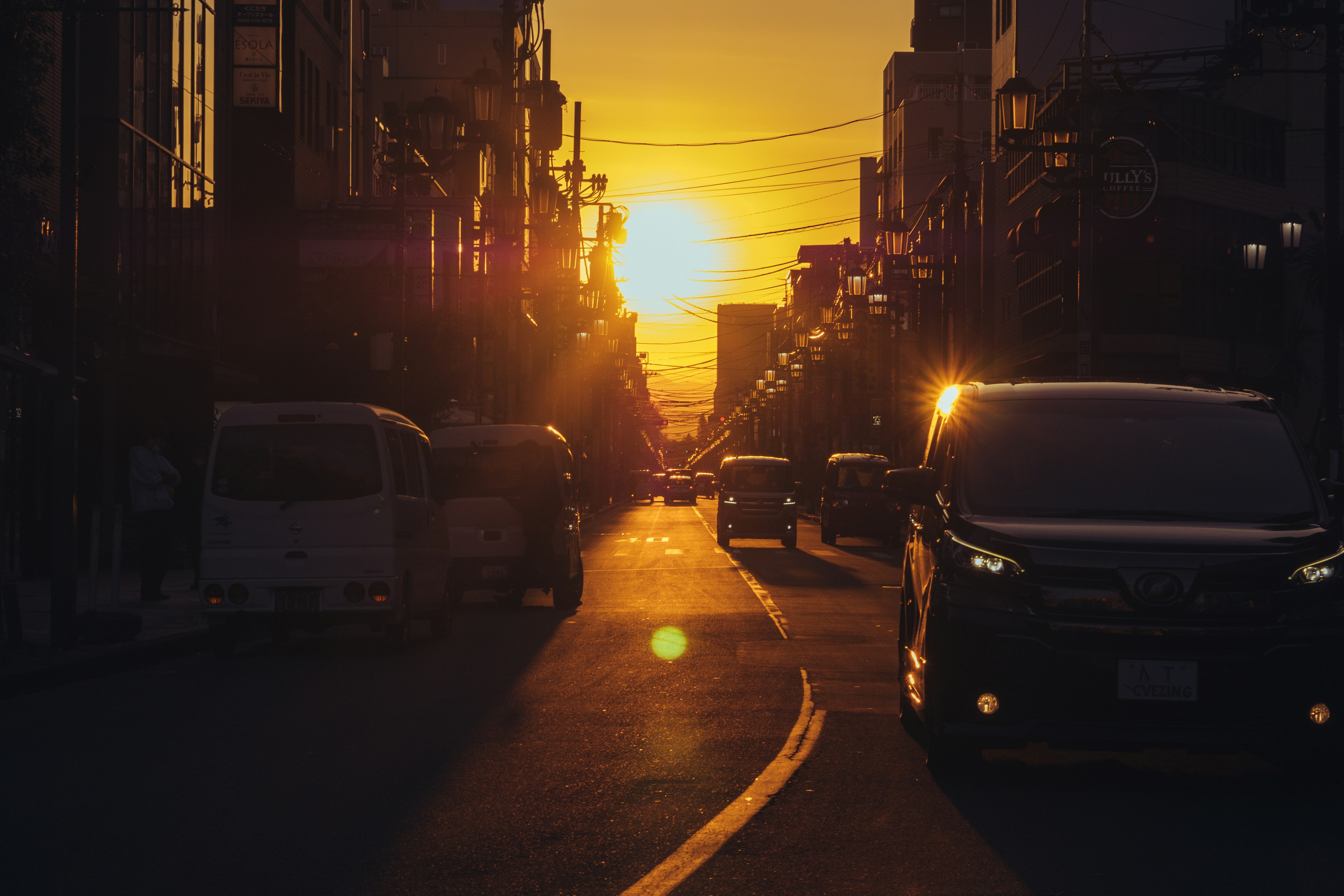 夕日が沈む都市の通りに並ぶ車と建物