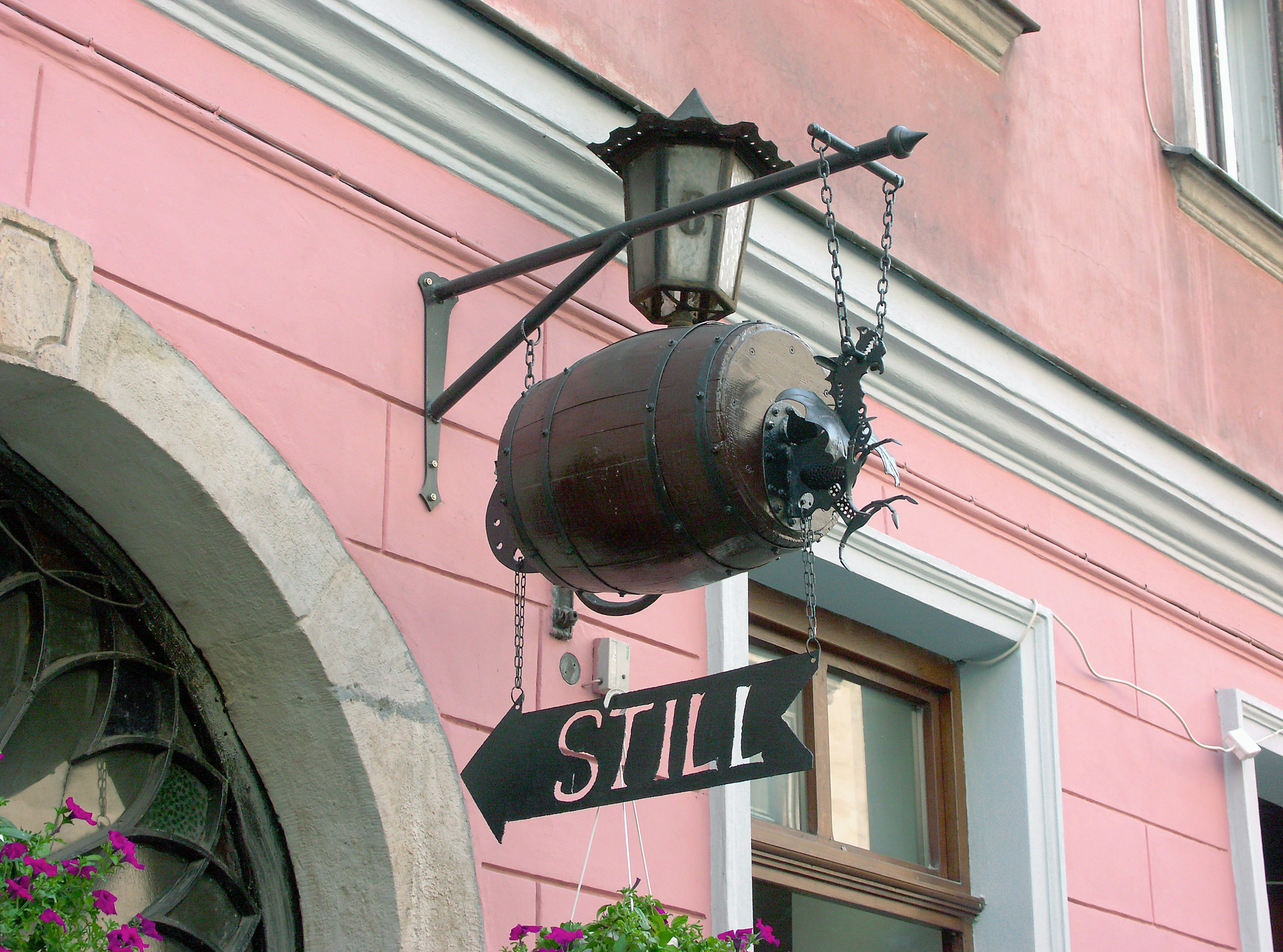 Une façade de magasin avec une lanterne et un panneau de baril ancien sur un mur rose