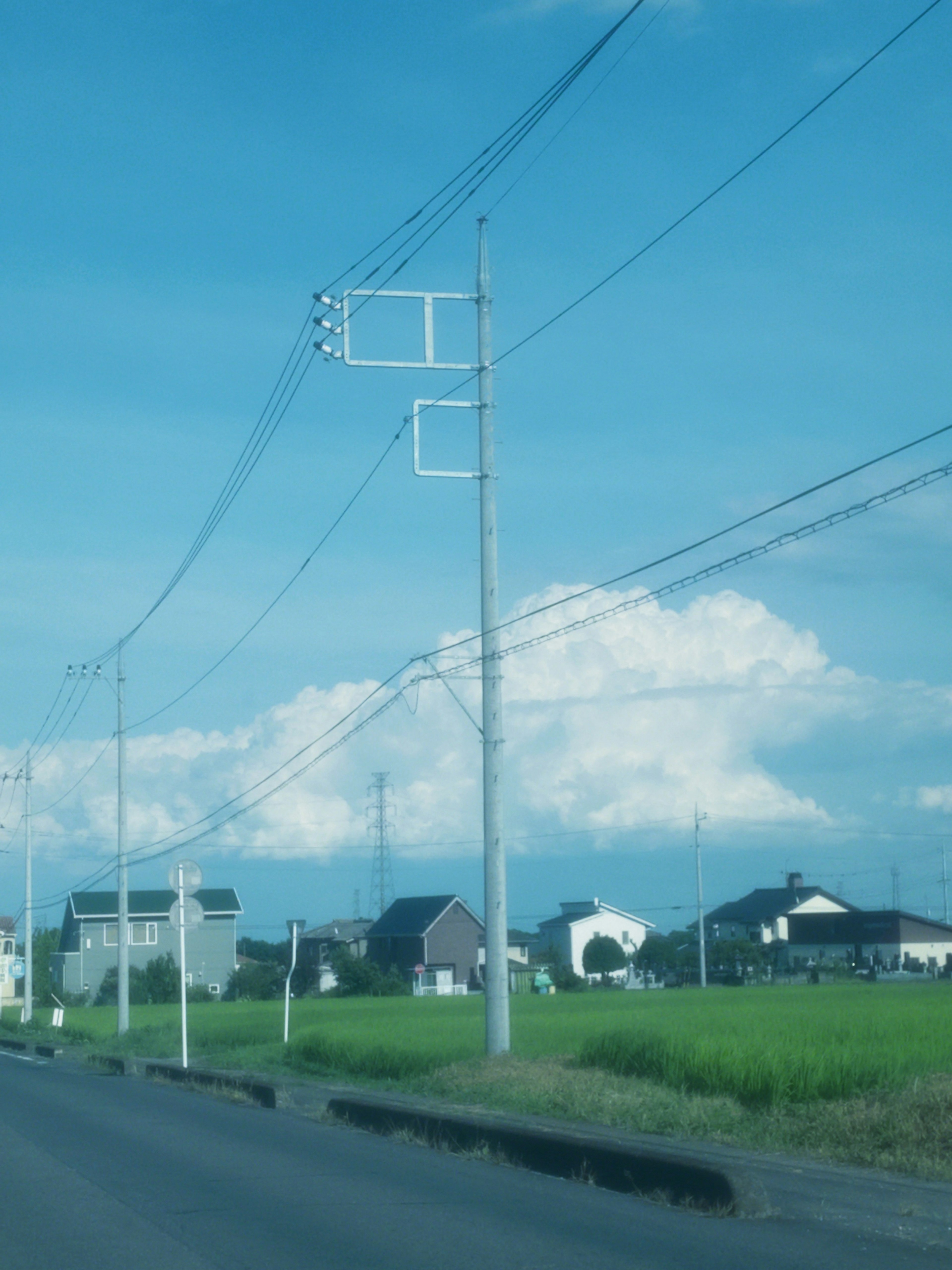 Ländliche Straße mit Strommasten unter einem blauen Himmel und weißen Wolken