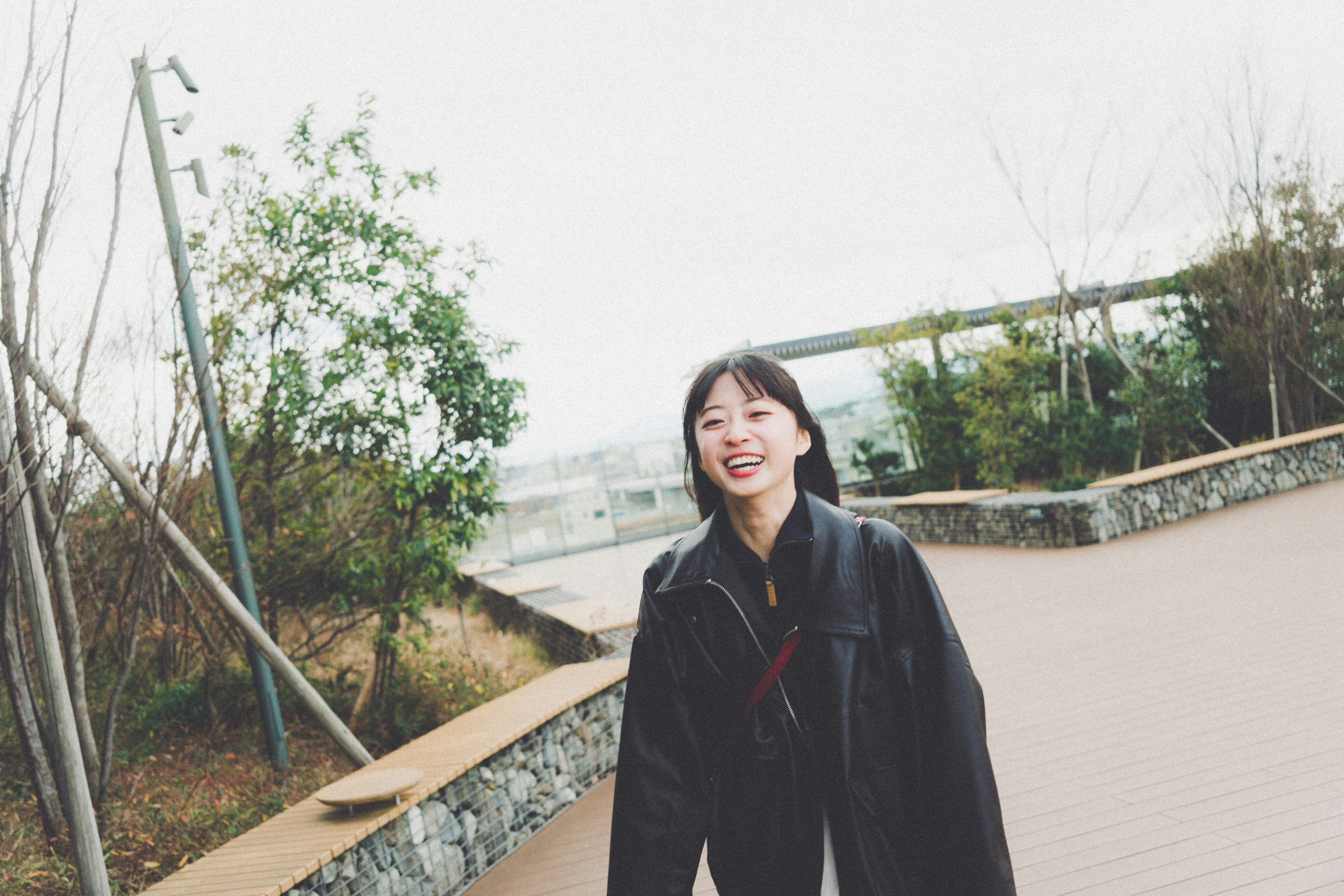 公園で笑顔の若い女性が黒いジャケットを着て立っている背景には緑の植物