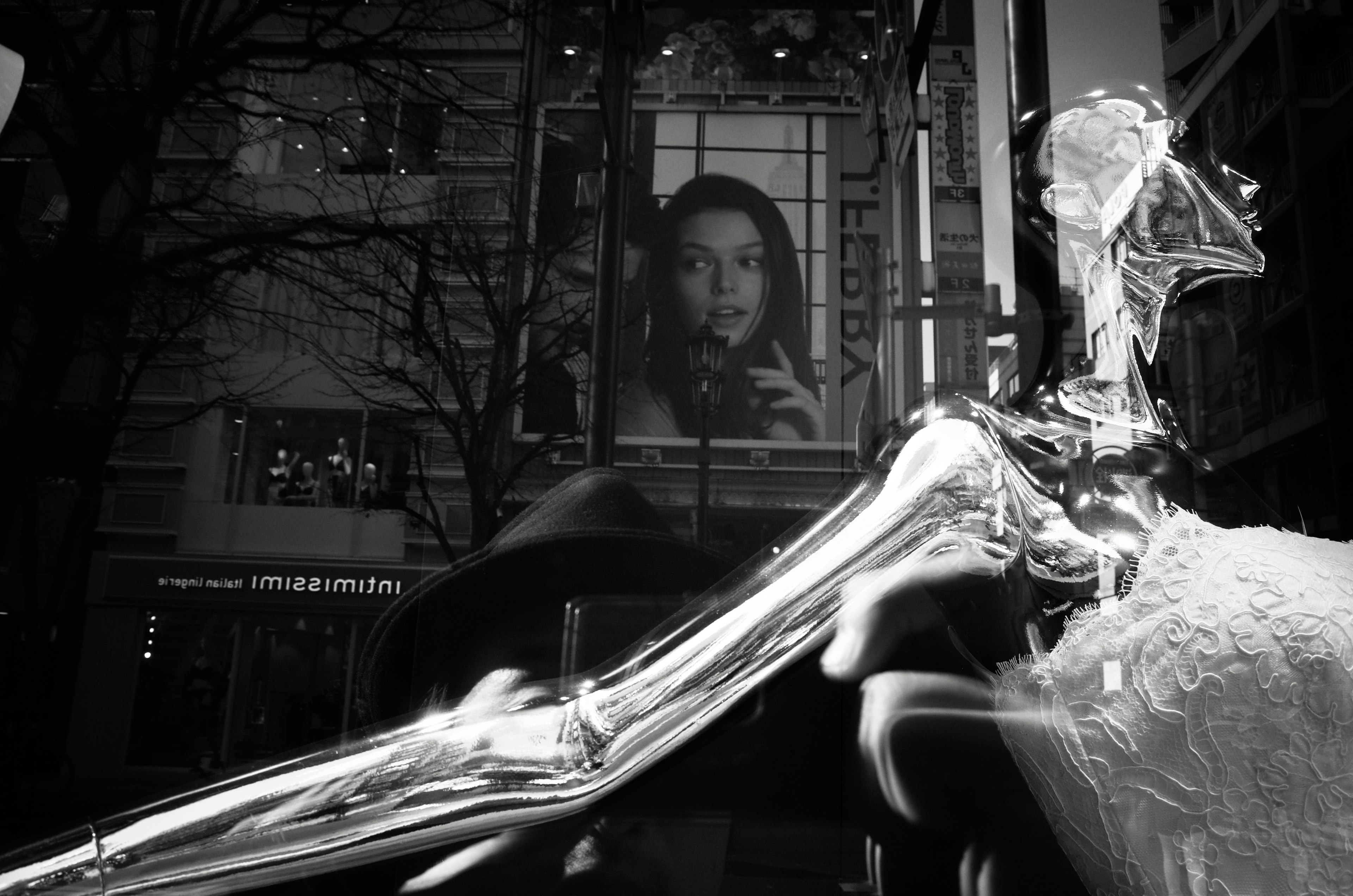 A transparent mannequin in a white dress with a large portrait of a woman in the background