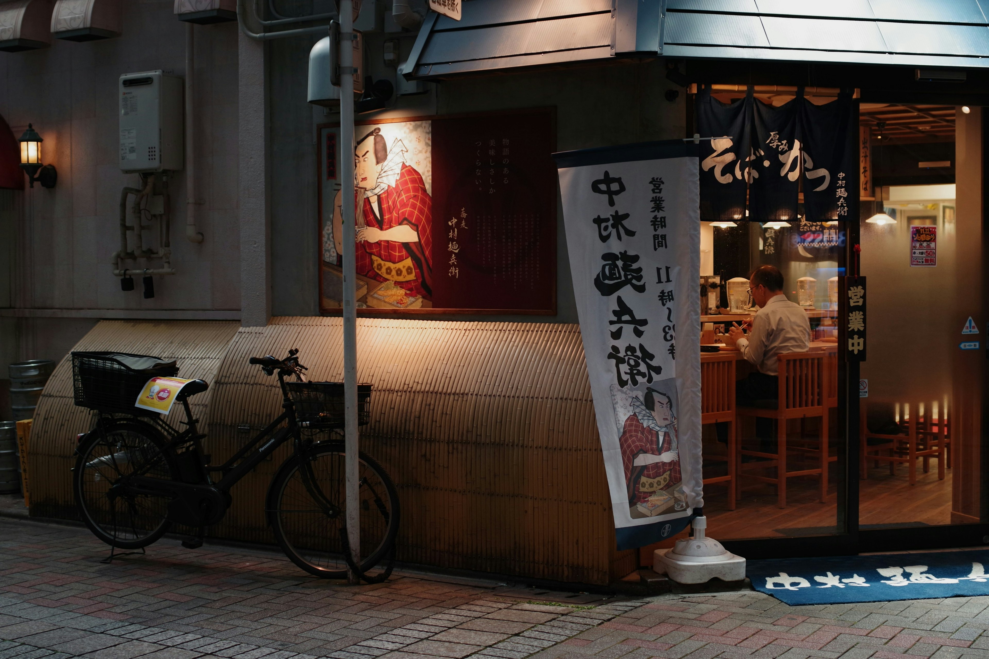 Exterior of a small eatery with a bicycle nearby Large sign next to the entrance Bright and warm atmosphere inside