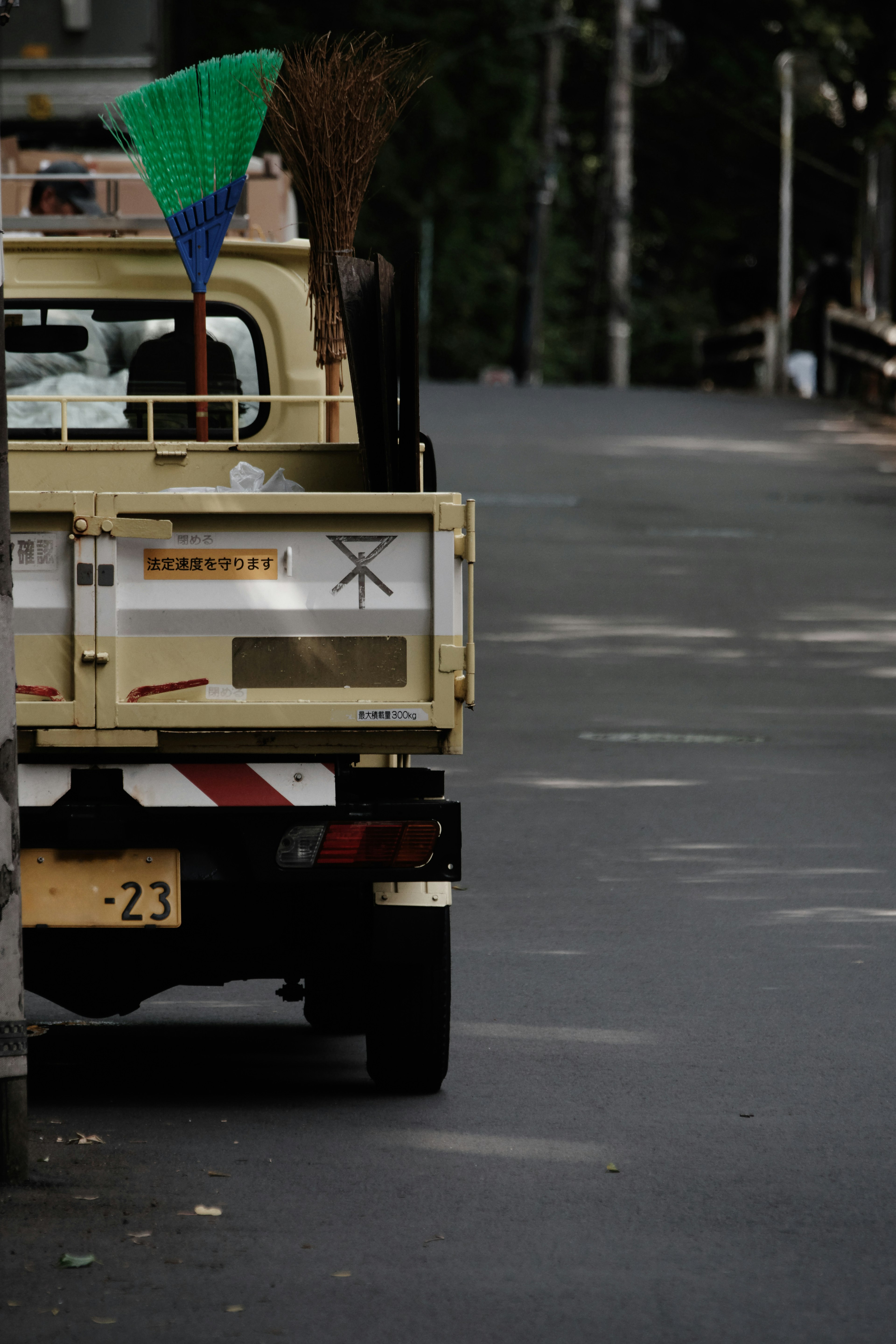 Back view of a cleaning vehicle parked on the road with a green and blue broom