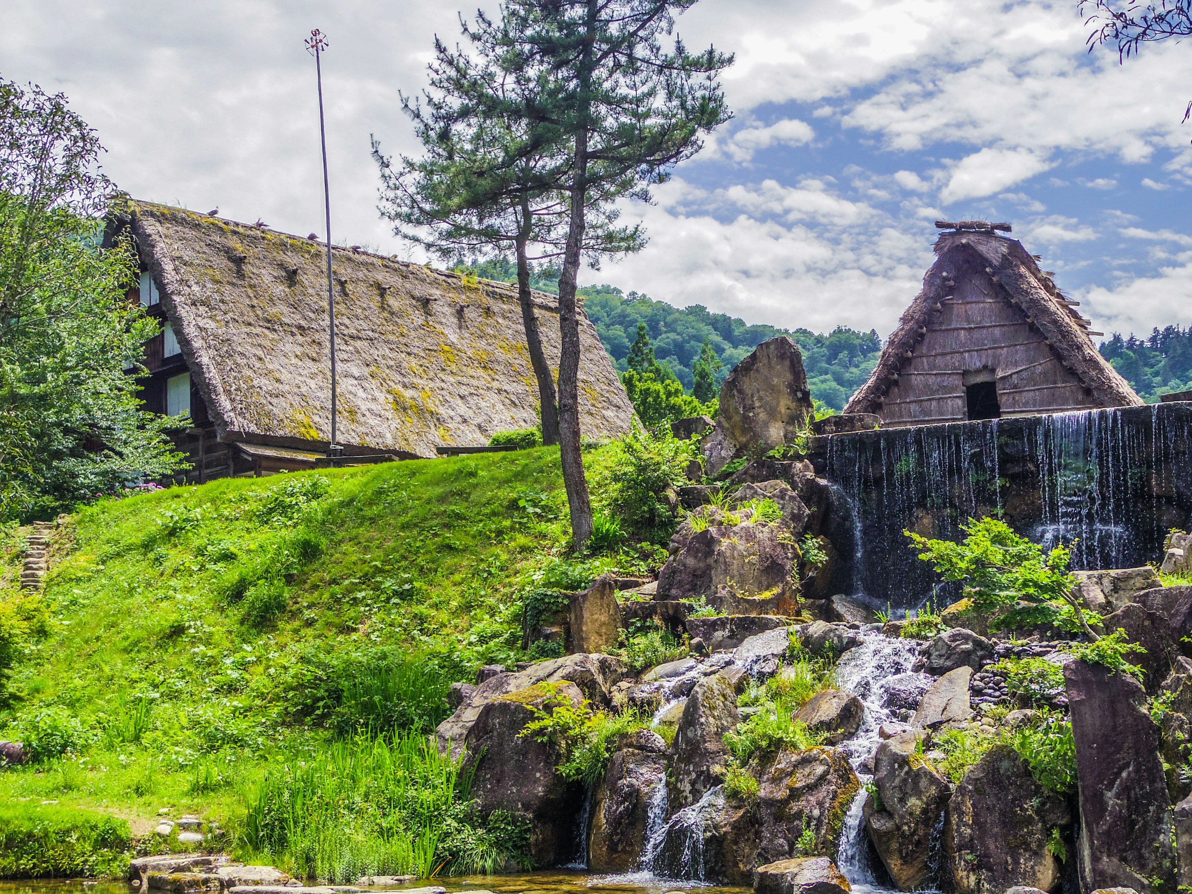 Pemandangan indah rumah tradisional atap jerami dan air terjun kecil di atas bukit hijau