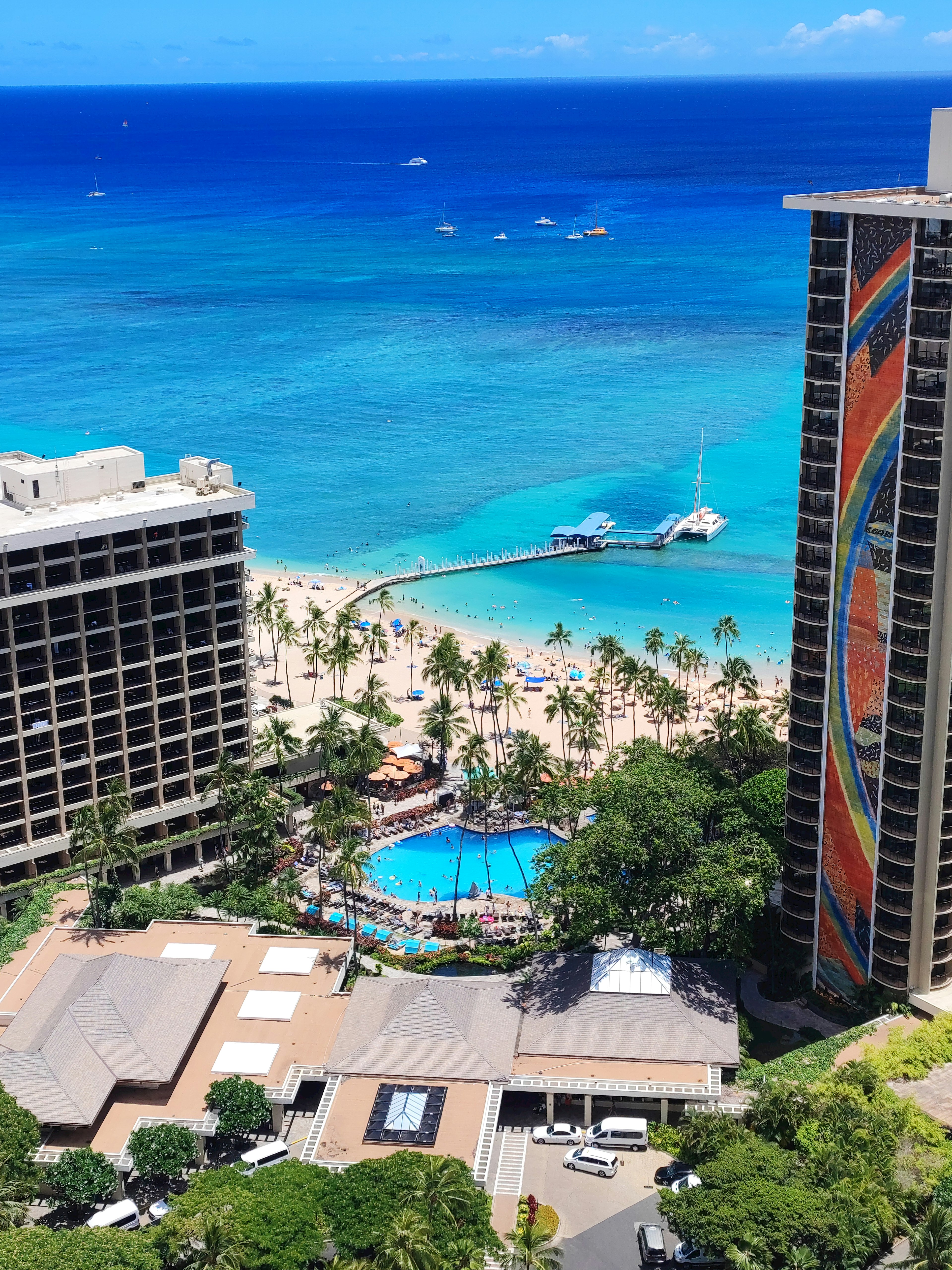 High-rise buildings overlooking a blue ocean and beach featuring a pool and palm trees