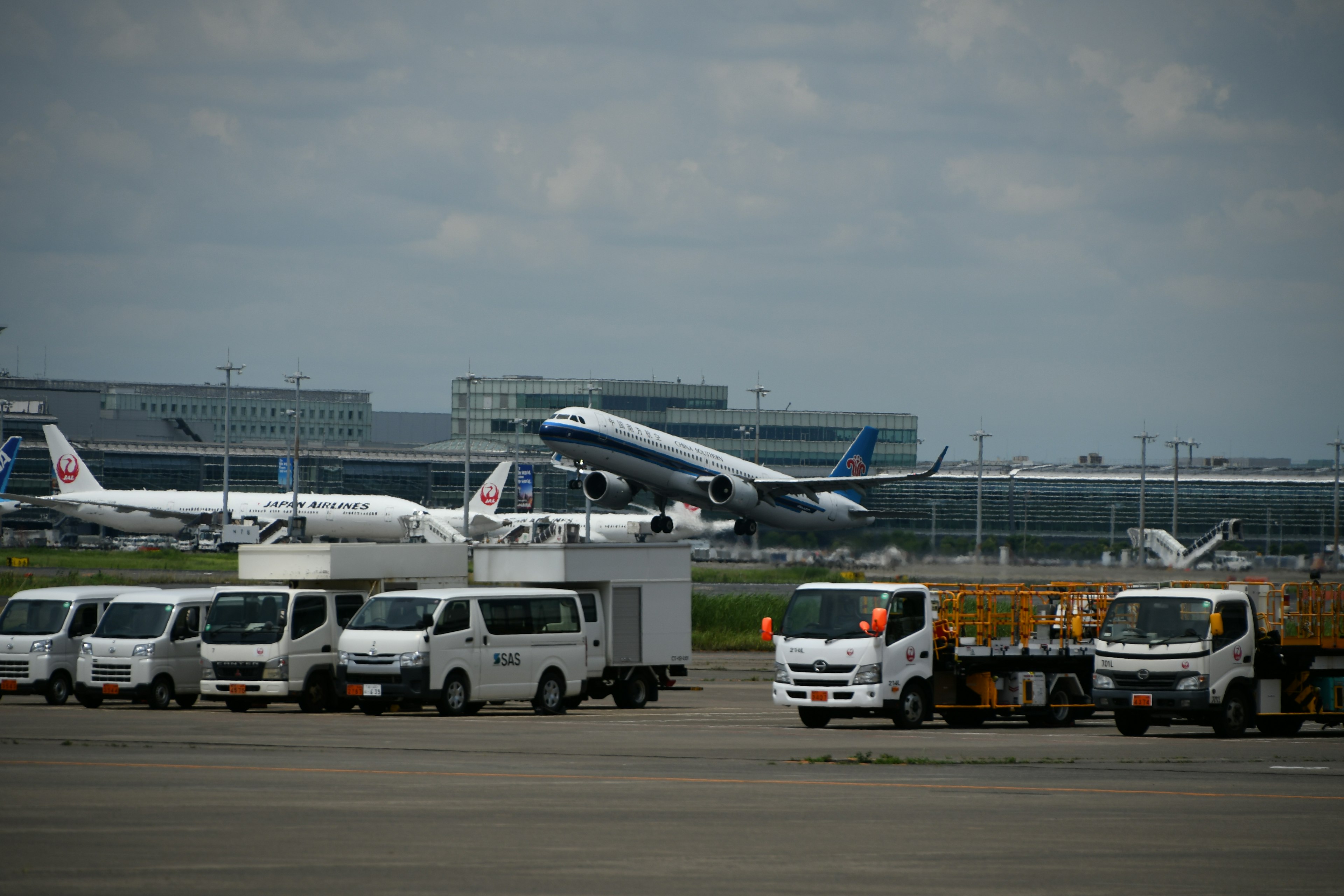 Flugzeug startet von einer Flughafenpiste mit geparkten Lastwagen