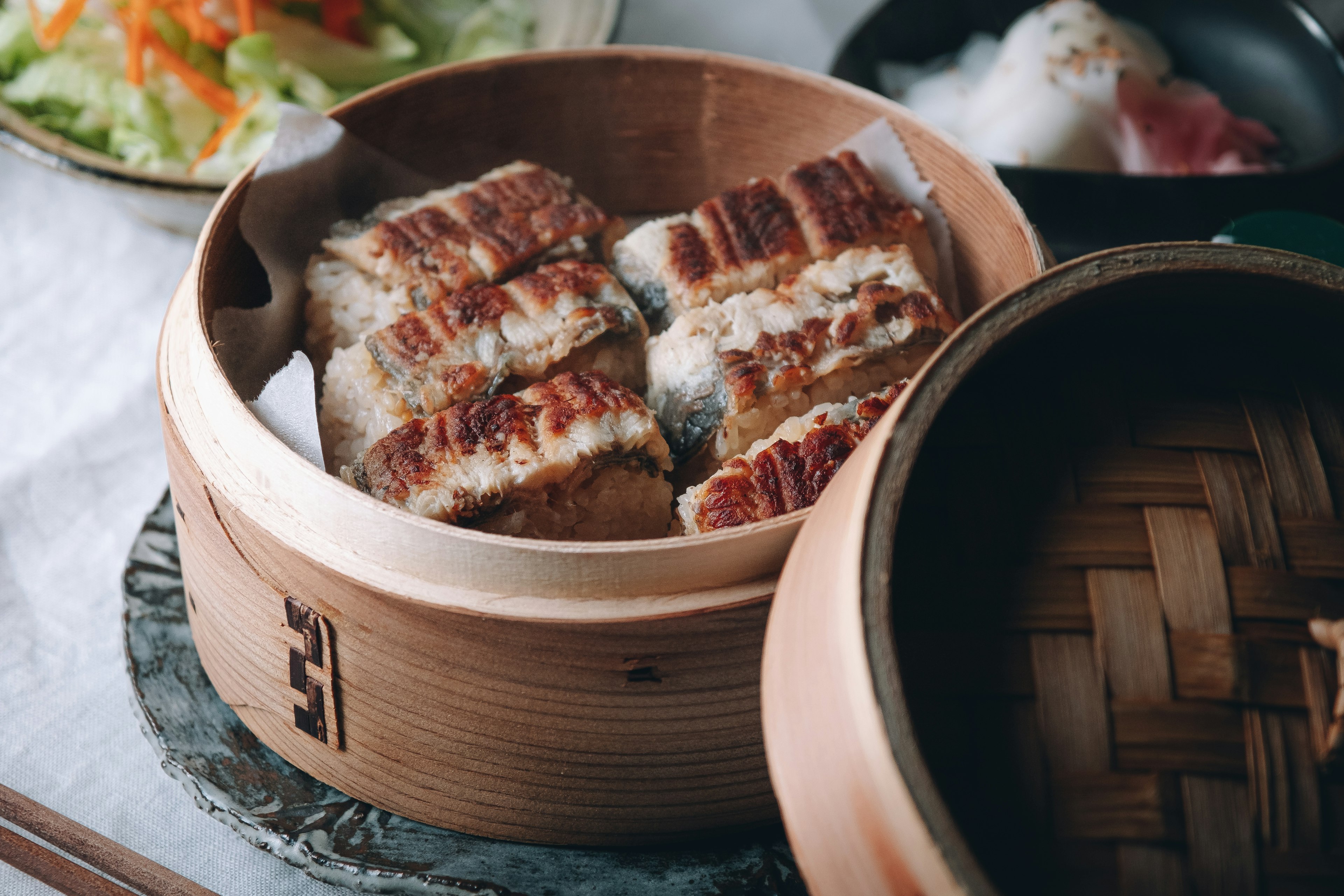 Steamed dish of grilled fish fillets in a bamboo steamer with salad and other dishes