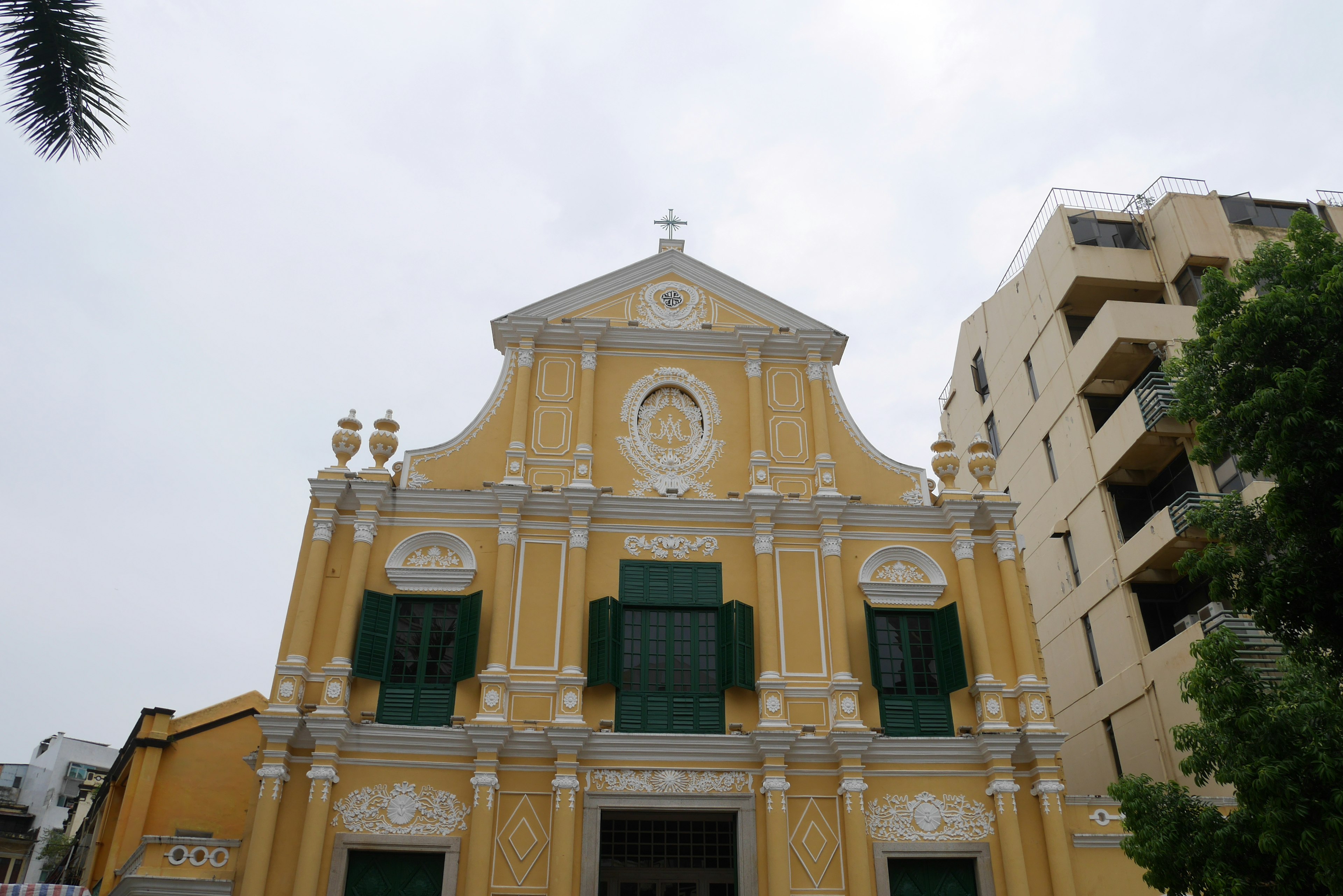 Fassade einer historischen Kirche mit gelbem Äußeren und grünen Fenstern mit aufwendigen Verzierungen