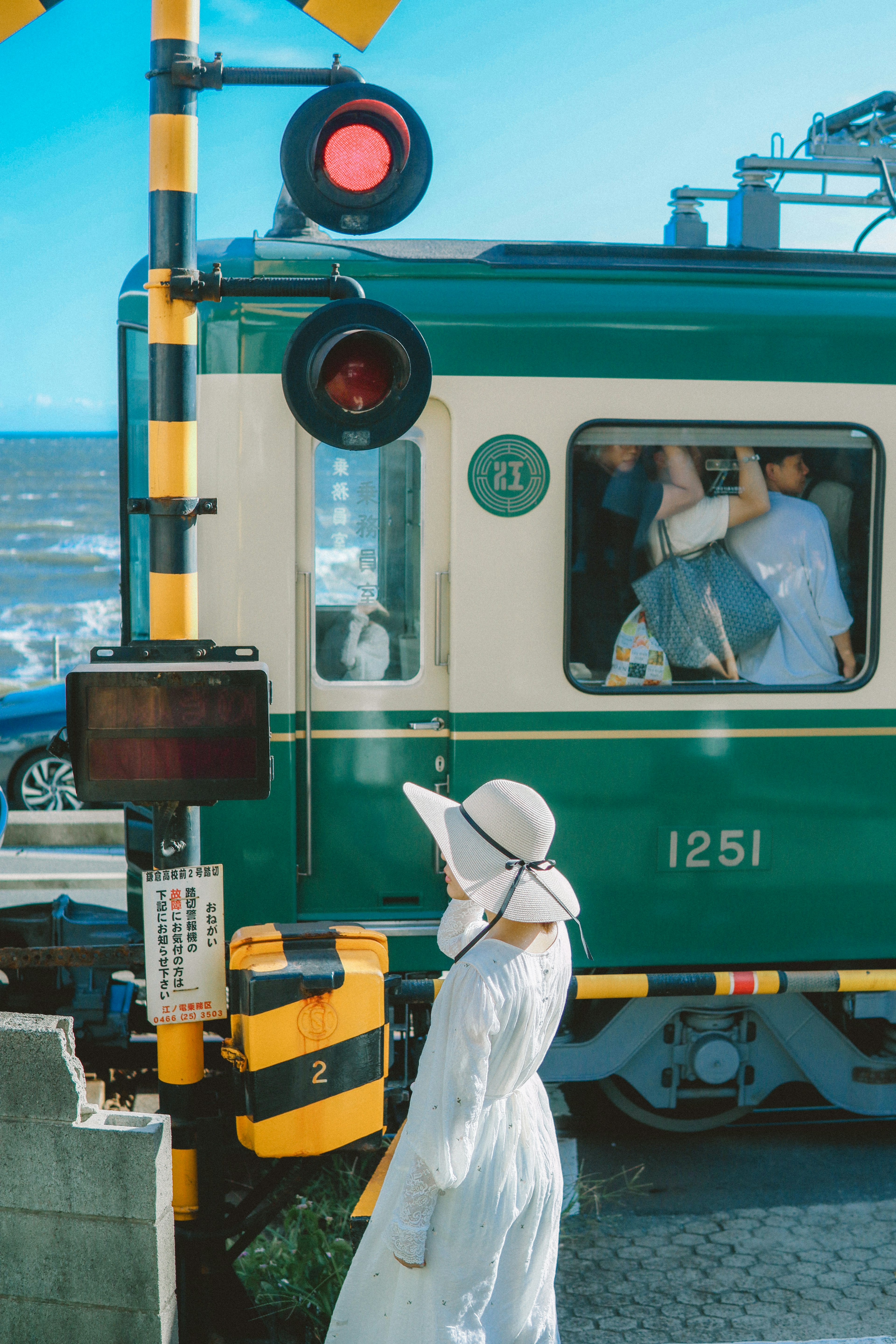 Green train passing by a woman in white clothing near the beach