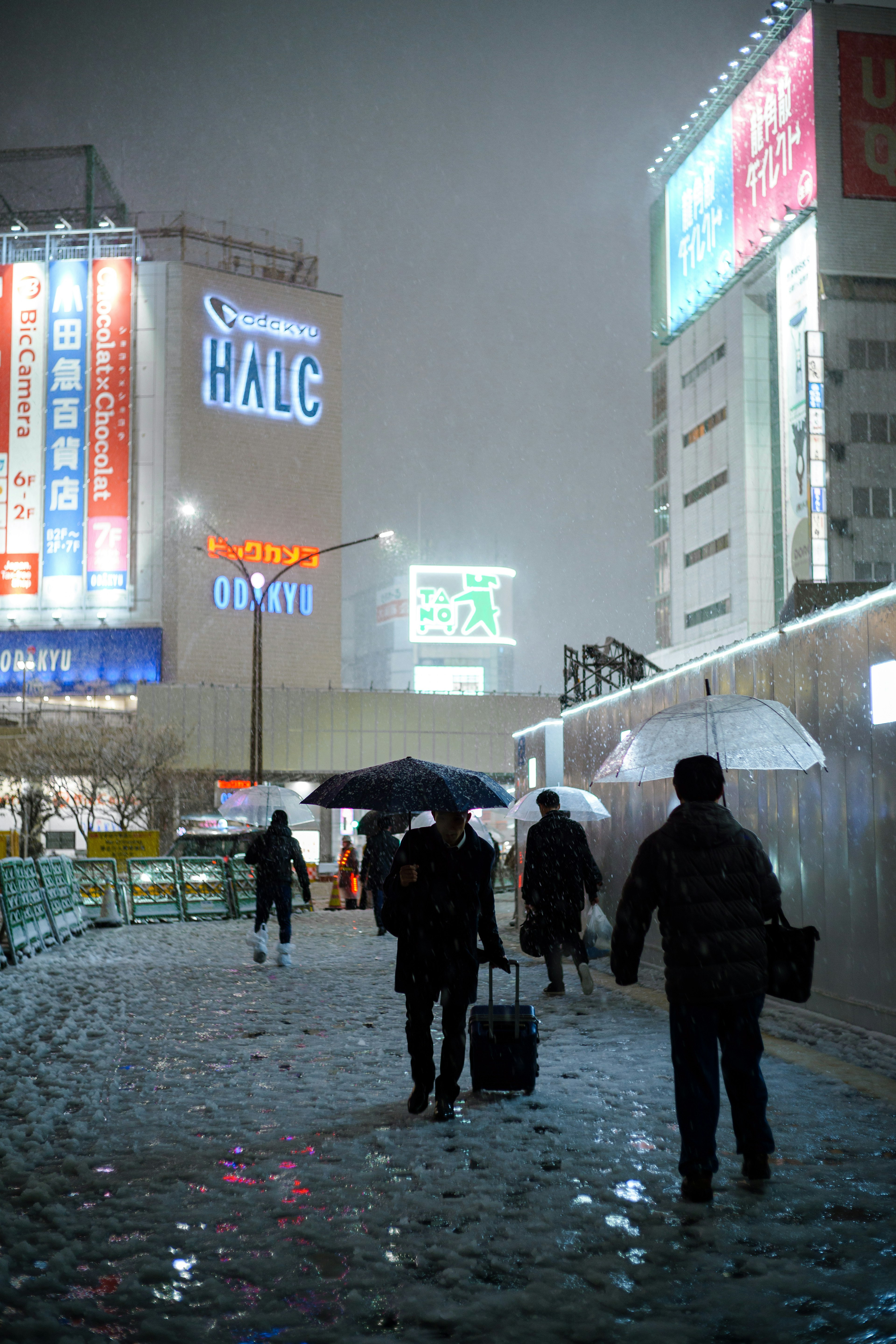 Des personnes marchant sous la neige avec des parapluies et des enseignes lumineuses en ville la nuit