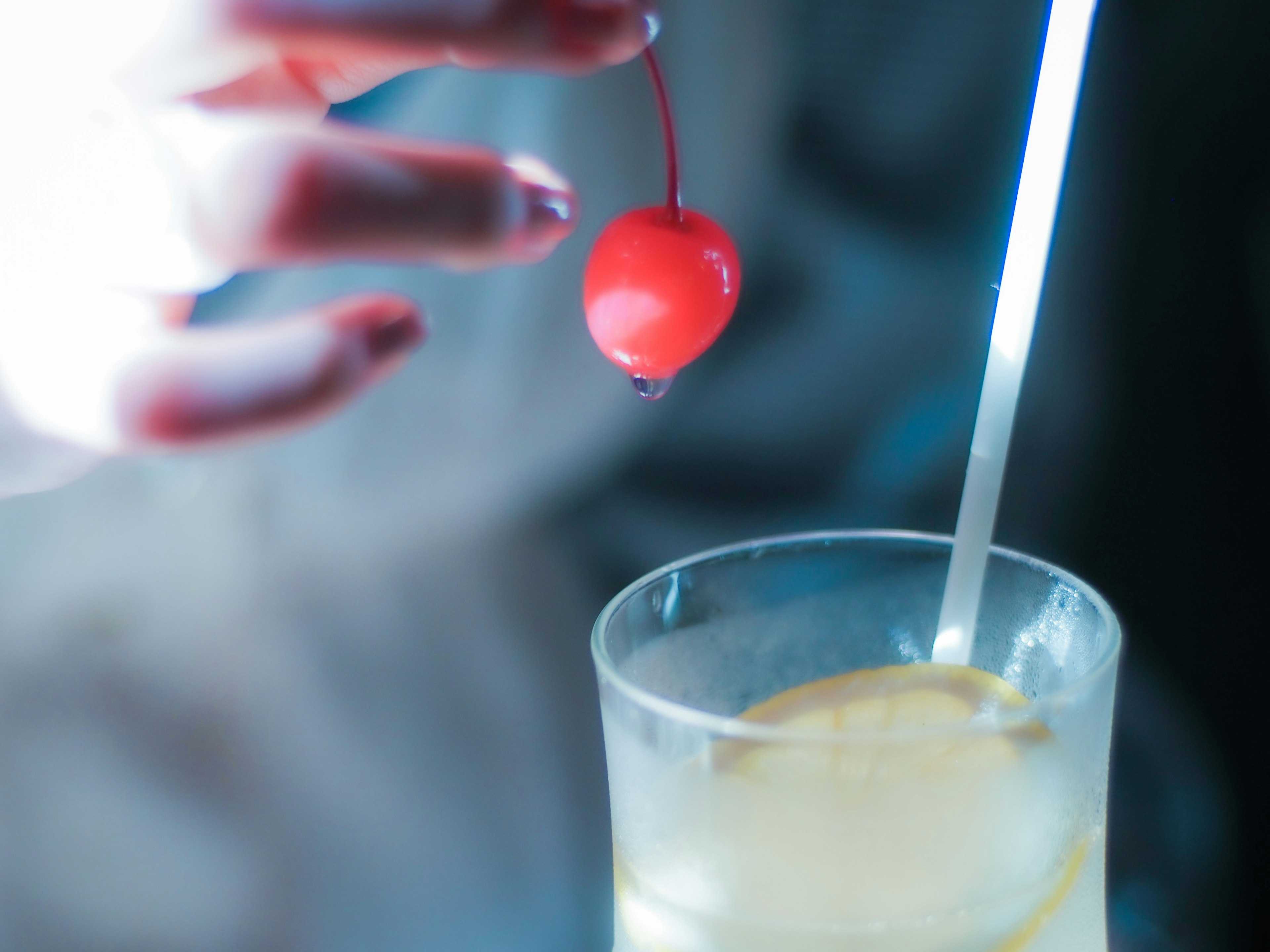 Hand holding a red cherry above a cocktail glass