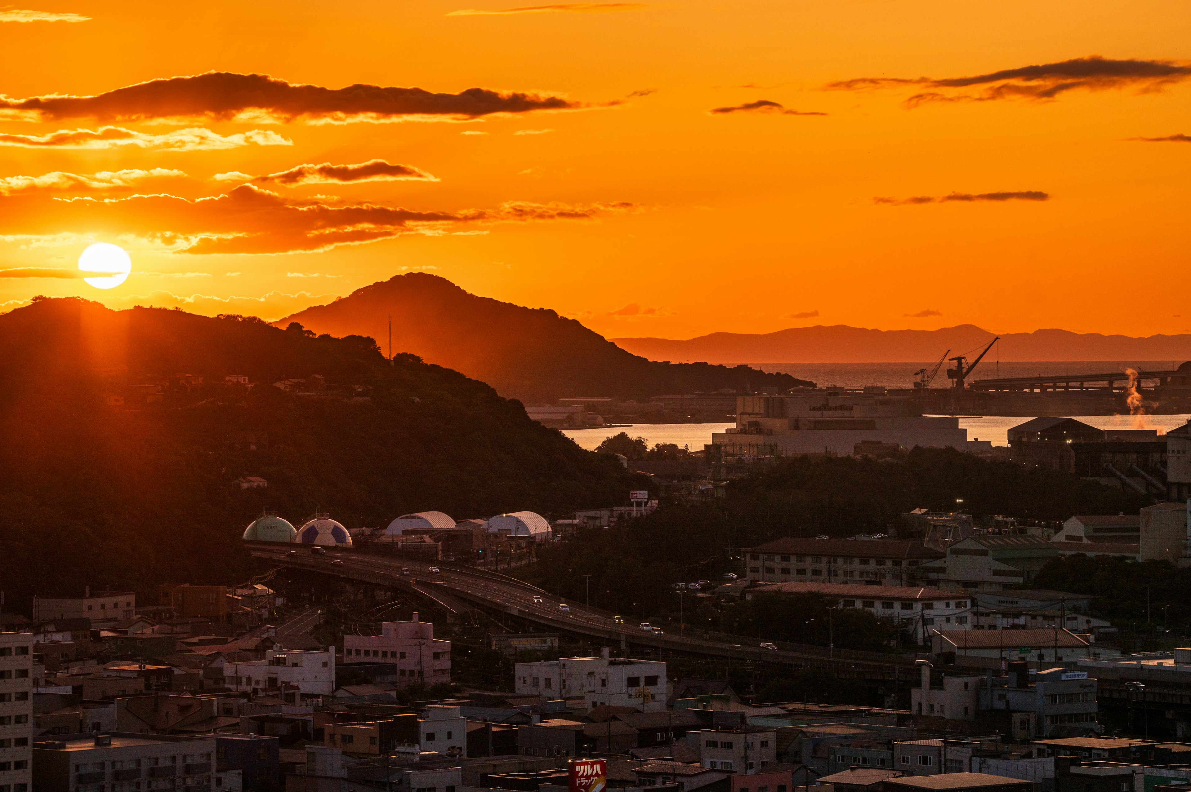 夕焼けの中に沈む太陽と山々を背景にした都市の風景