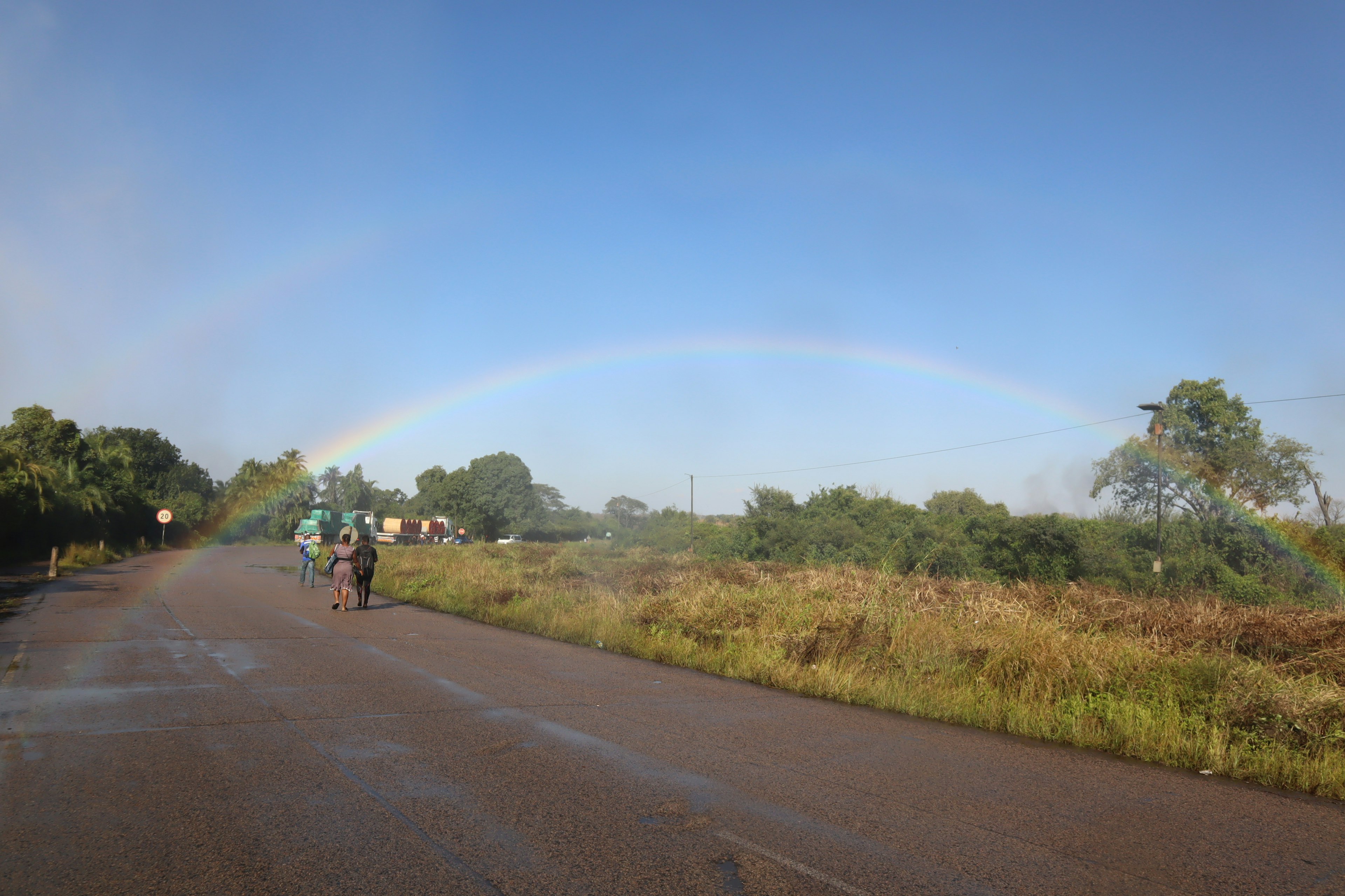 Ein Regenbogen unter einem klaren Himmel mit einer nassen Straße und Radfahrern