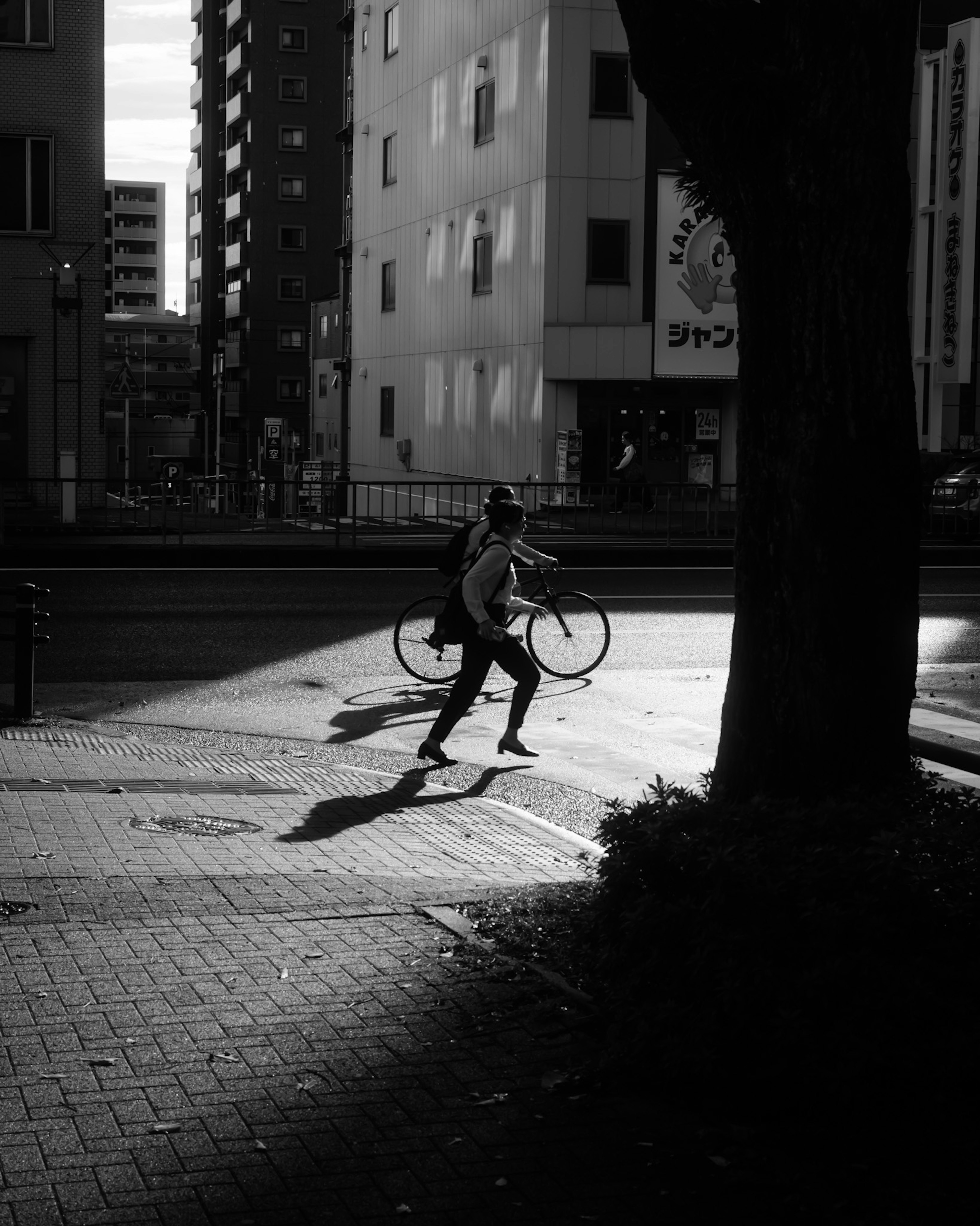 Une scène urbaine en noir et blanc contrasté avec une personne courant en tenant un vélo