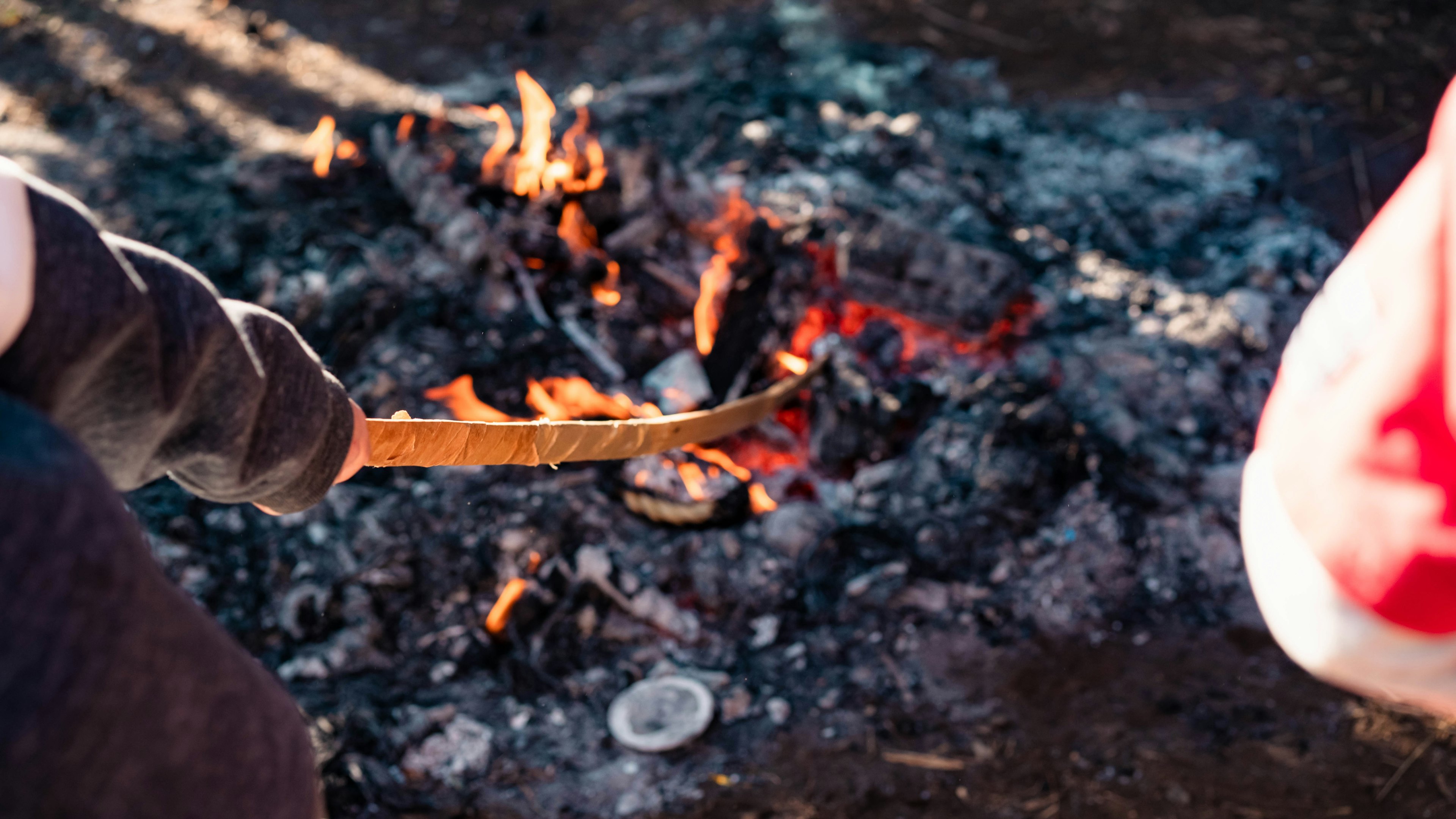 Hand, die ein gebogenes Messer über ein Feuer mit glühenden Kohlen hält