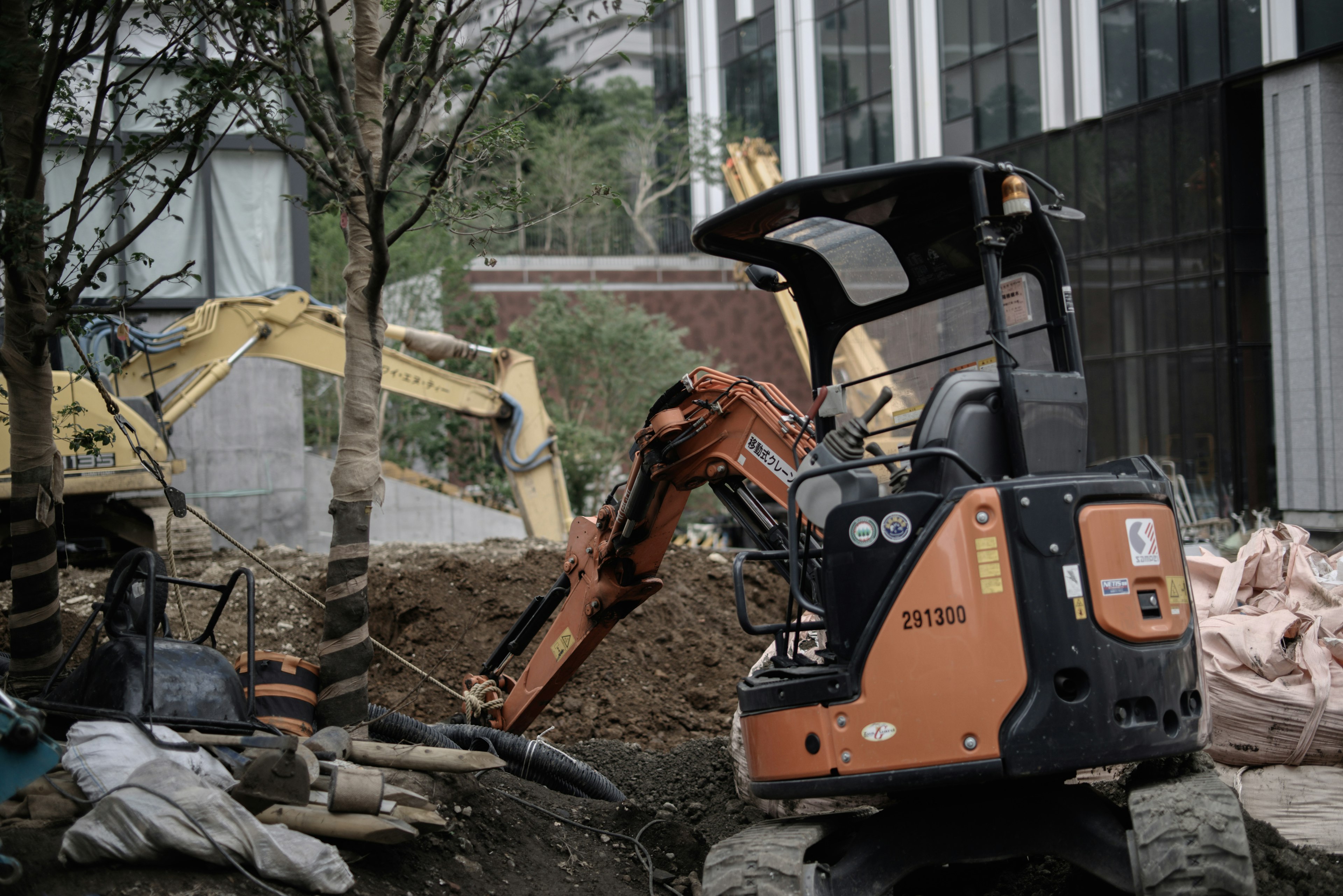 Imagen de un sitio de construcción con maquinaria pesada que incluye una mini excavadora y una máquina más grande al fondo