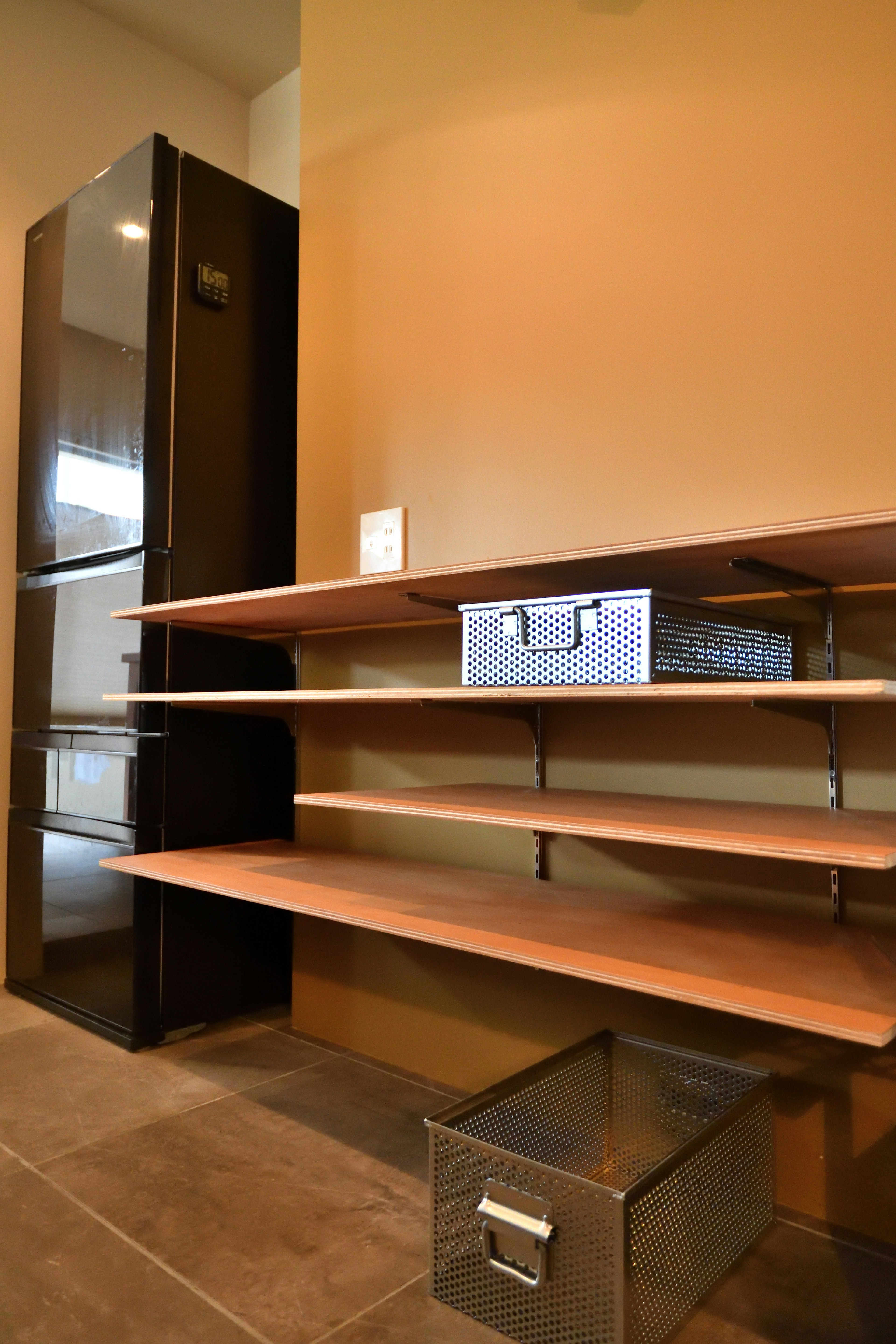 Modern kitchen storage space with wooden shelves and metal drawer next to a refrigerator