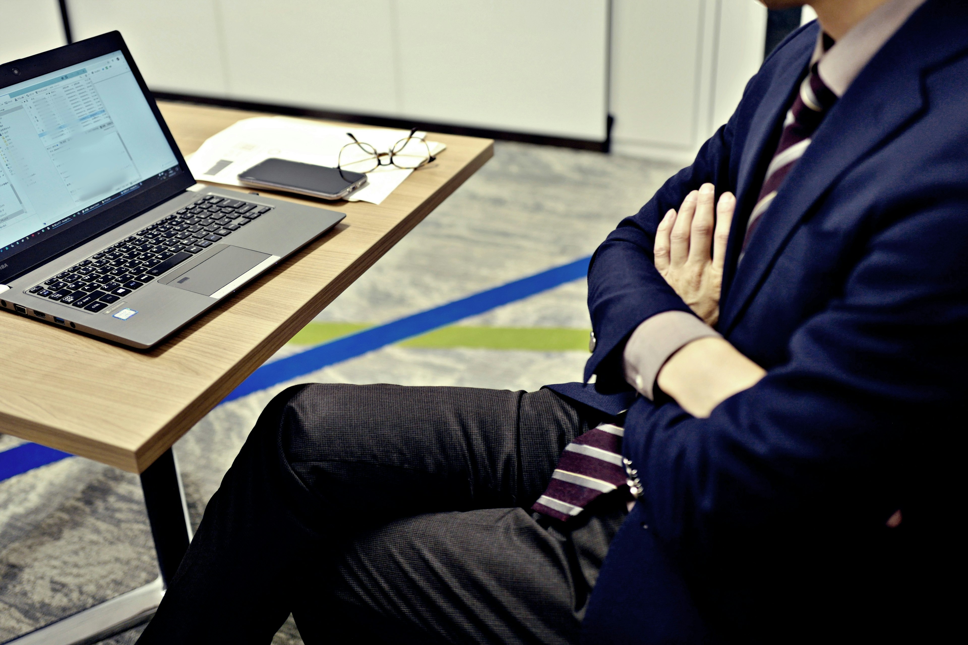 Businessman sitting at a desk with a laptop arms crossed wearing a suit