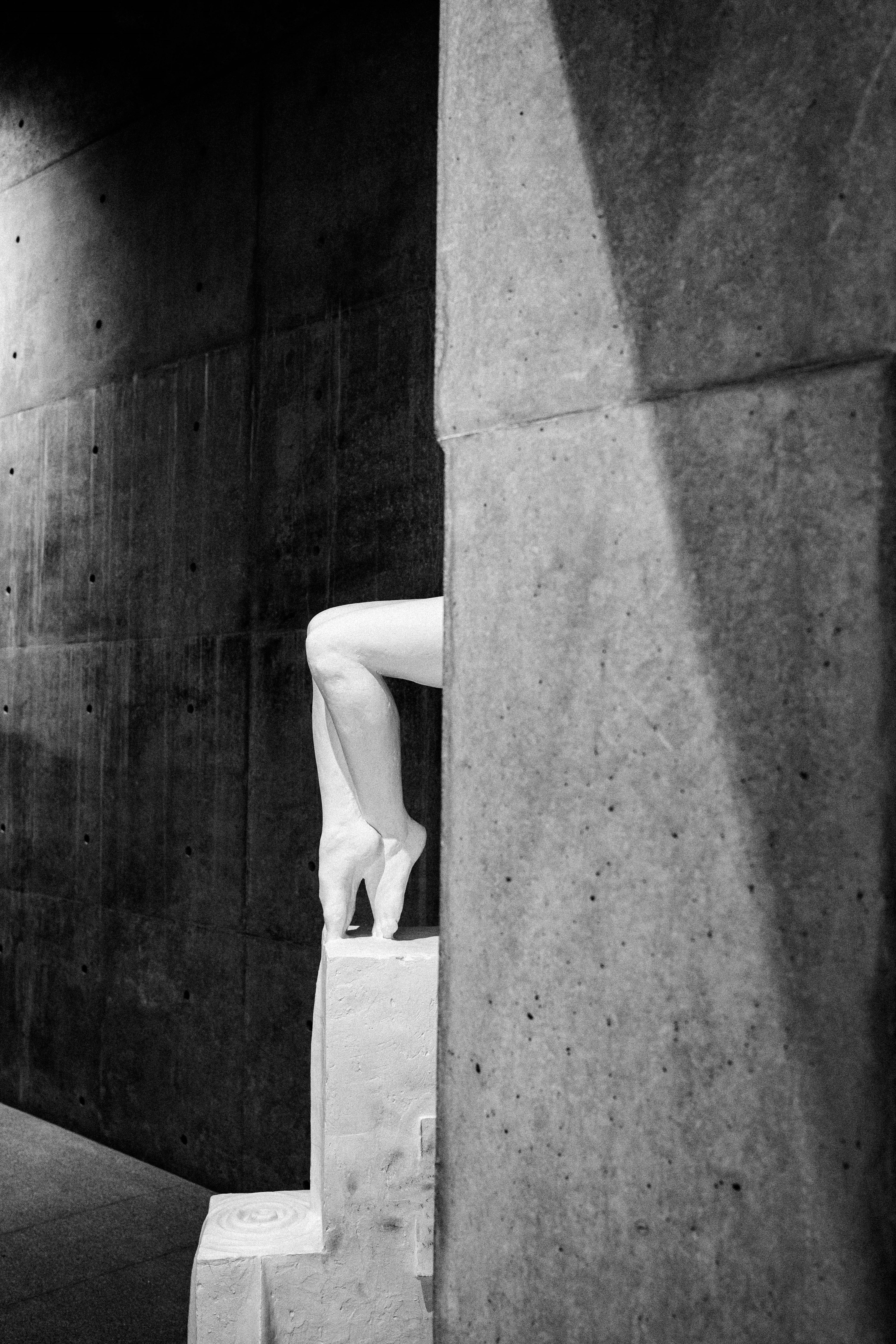 Une jambe blanche en talons hauts partiellement visible derrière un mur en béton