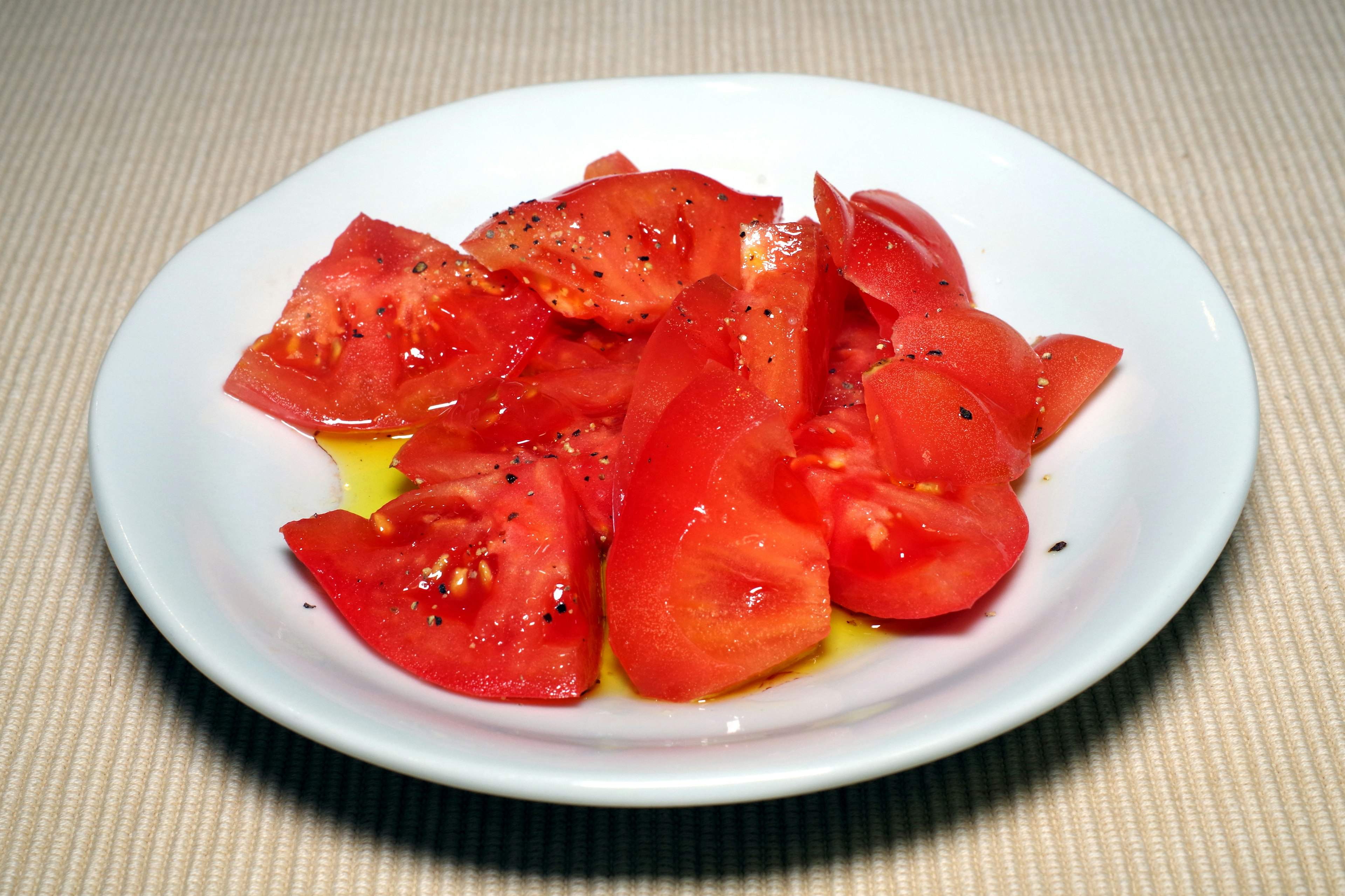 Sliced red tomatoes drizzled with olive oil on a white plate