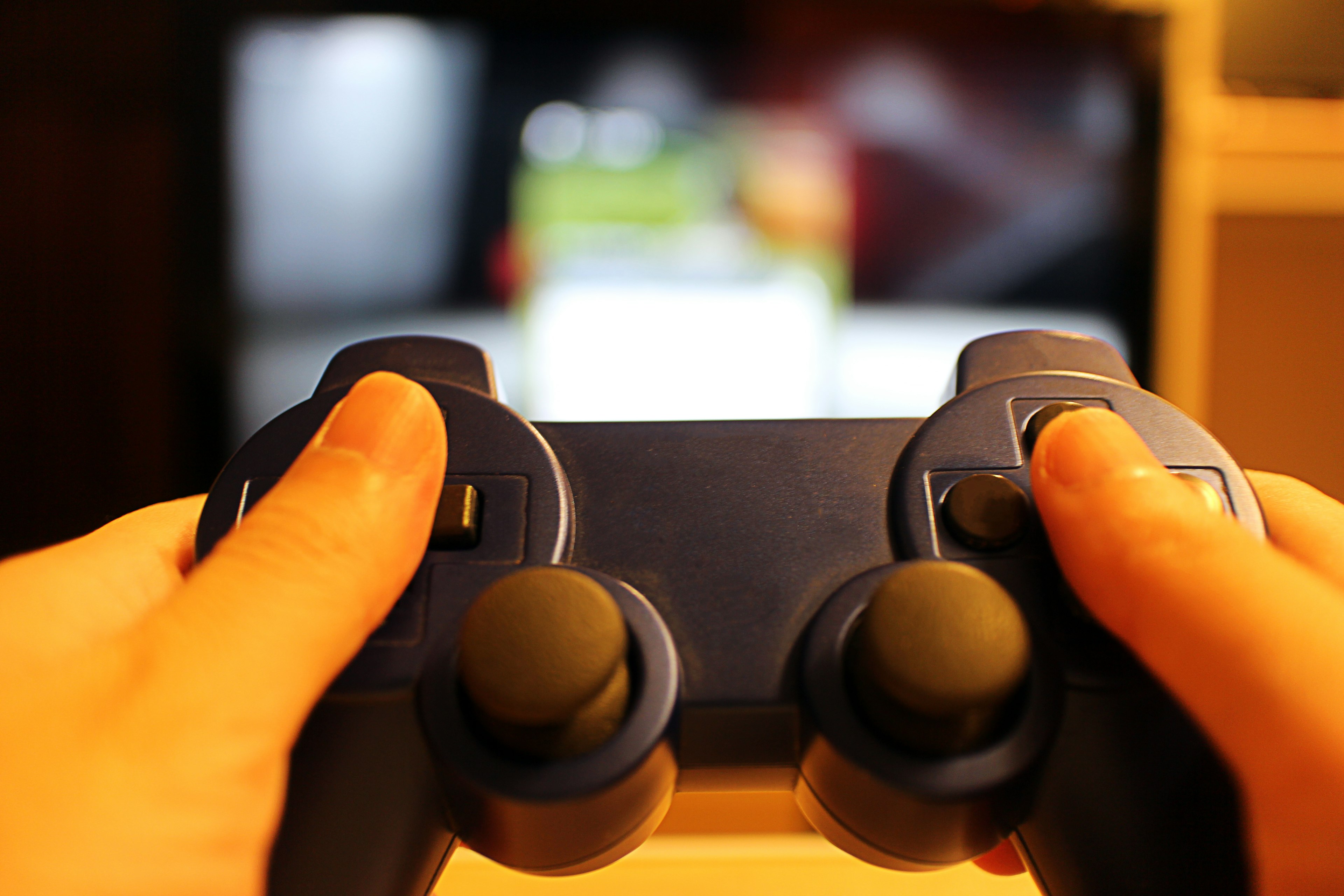 Mains tenant une manette de jeu bleue avec un écran de télévision en arrière-plan