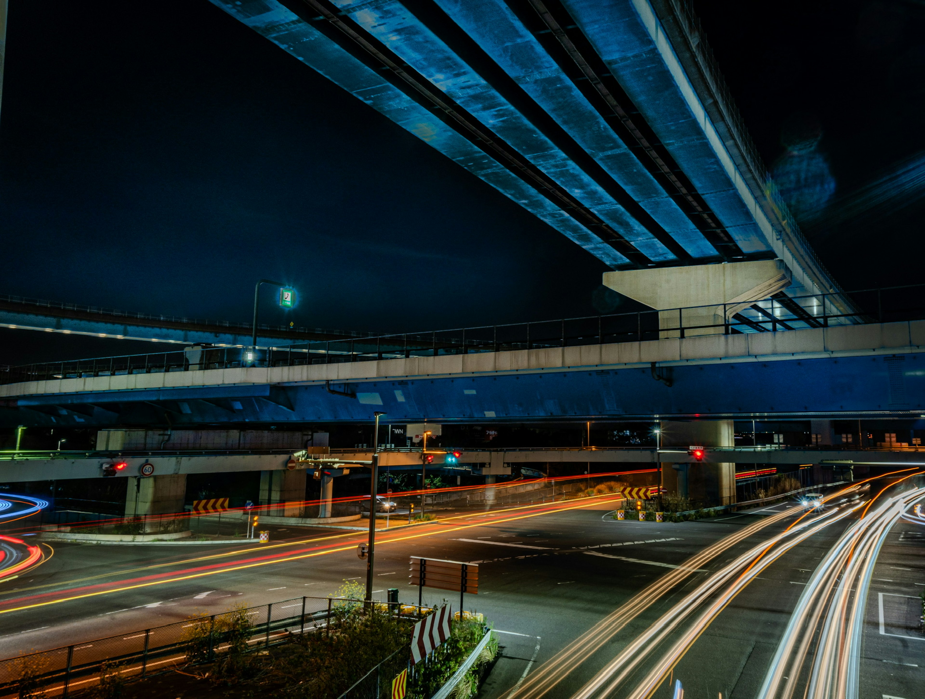 Paesaggio urbano notturno con autostrade elevate che si incrociano scie di luce dei veicoli e ponte blu