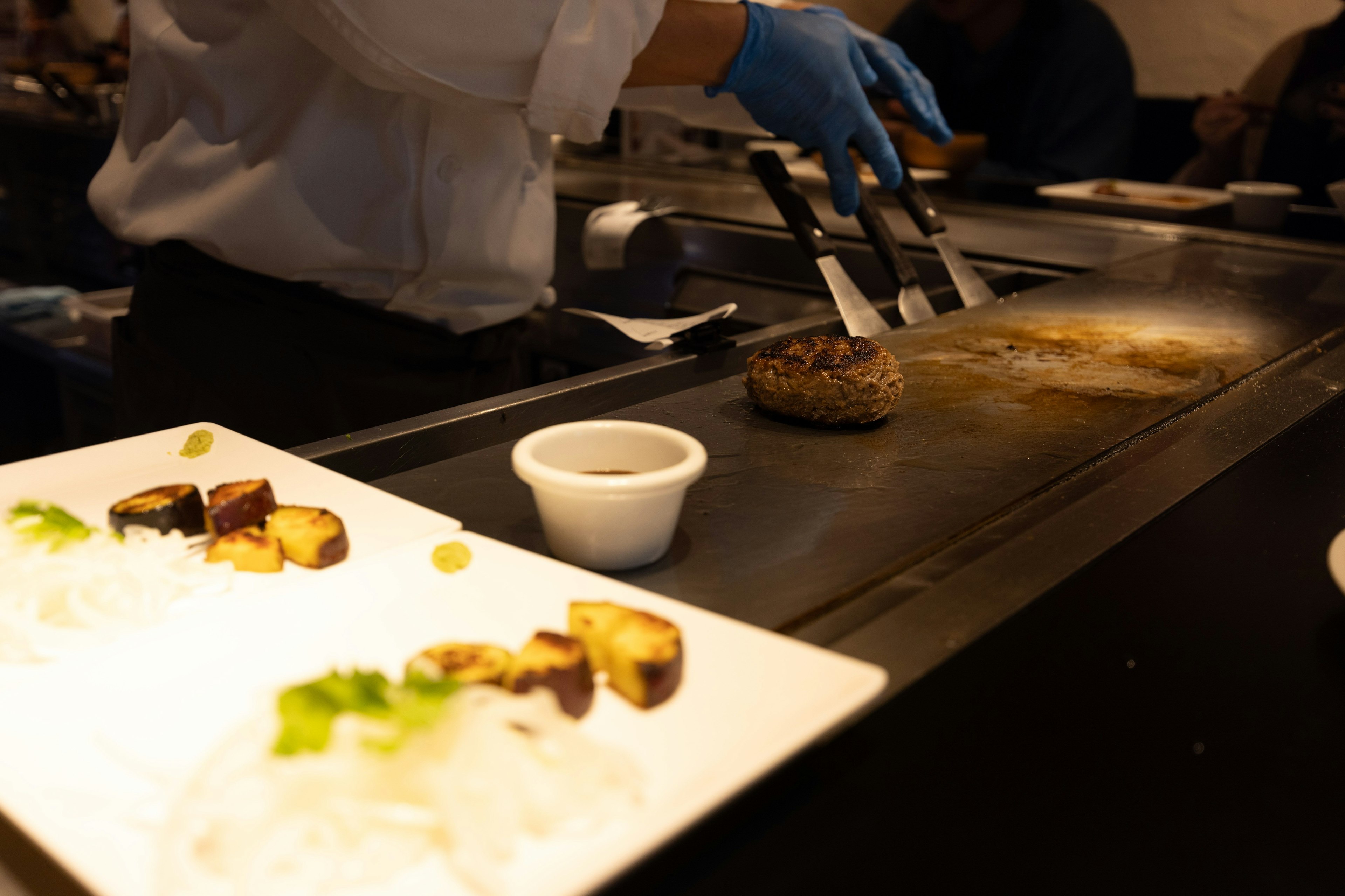 Koch, der auf einem Teppanyaki-Grill kocht, mit angerichtetem Essen und Sauce