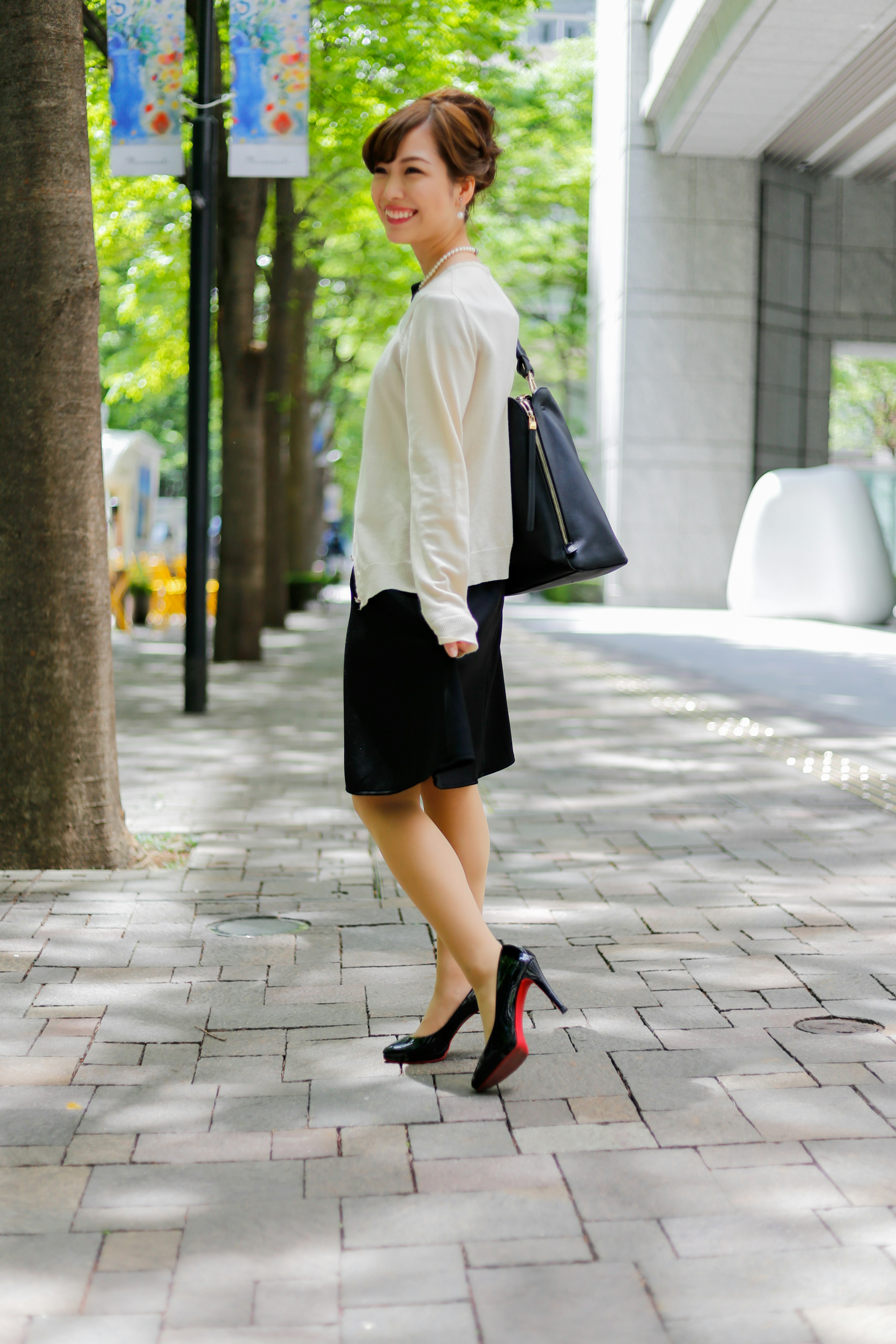 Woman walking in a black skirt and white sweater on a city street