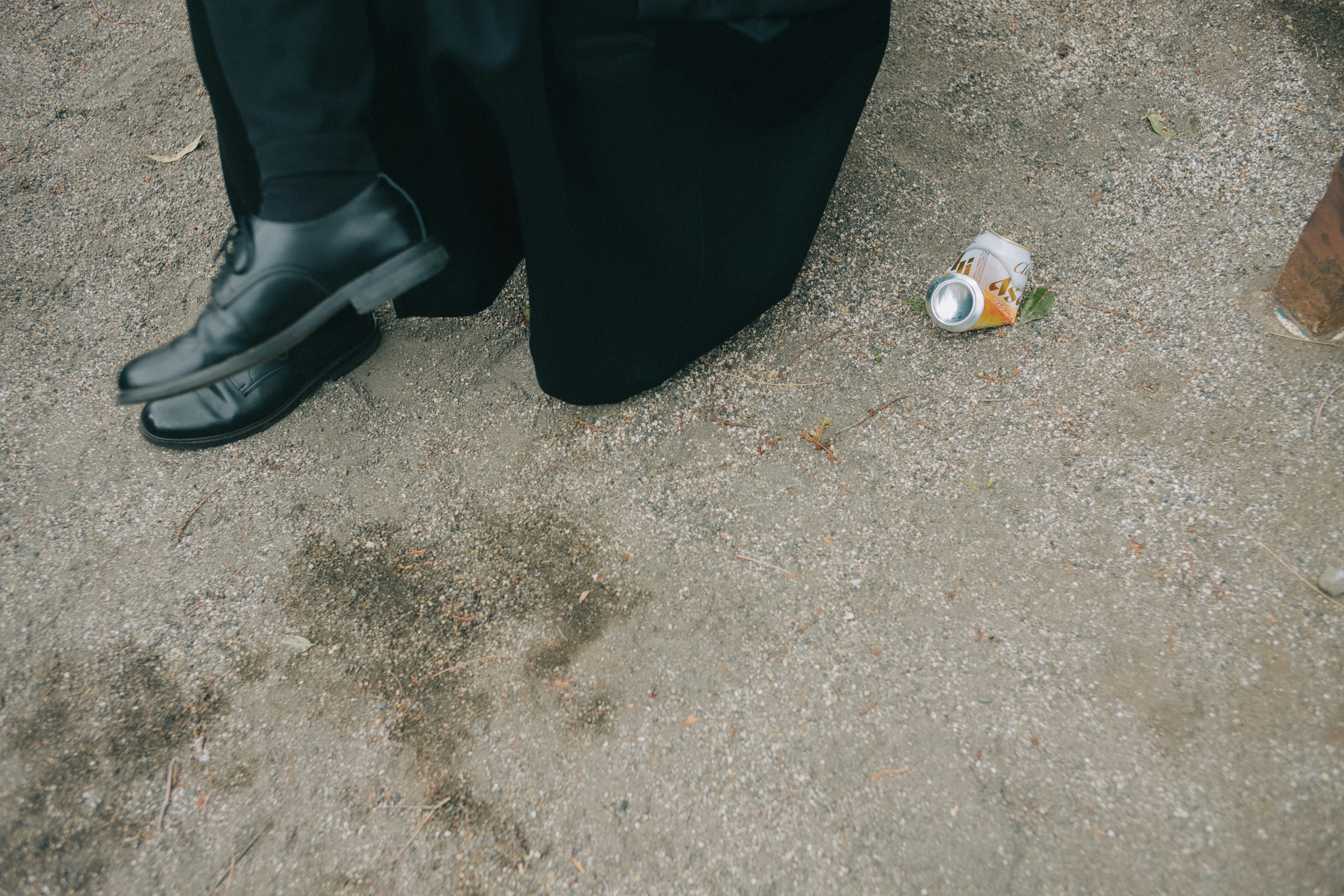 Feet of a person in black clothing with a discarded can on the ground