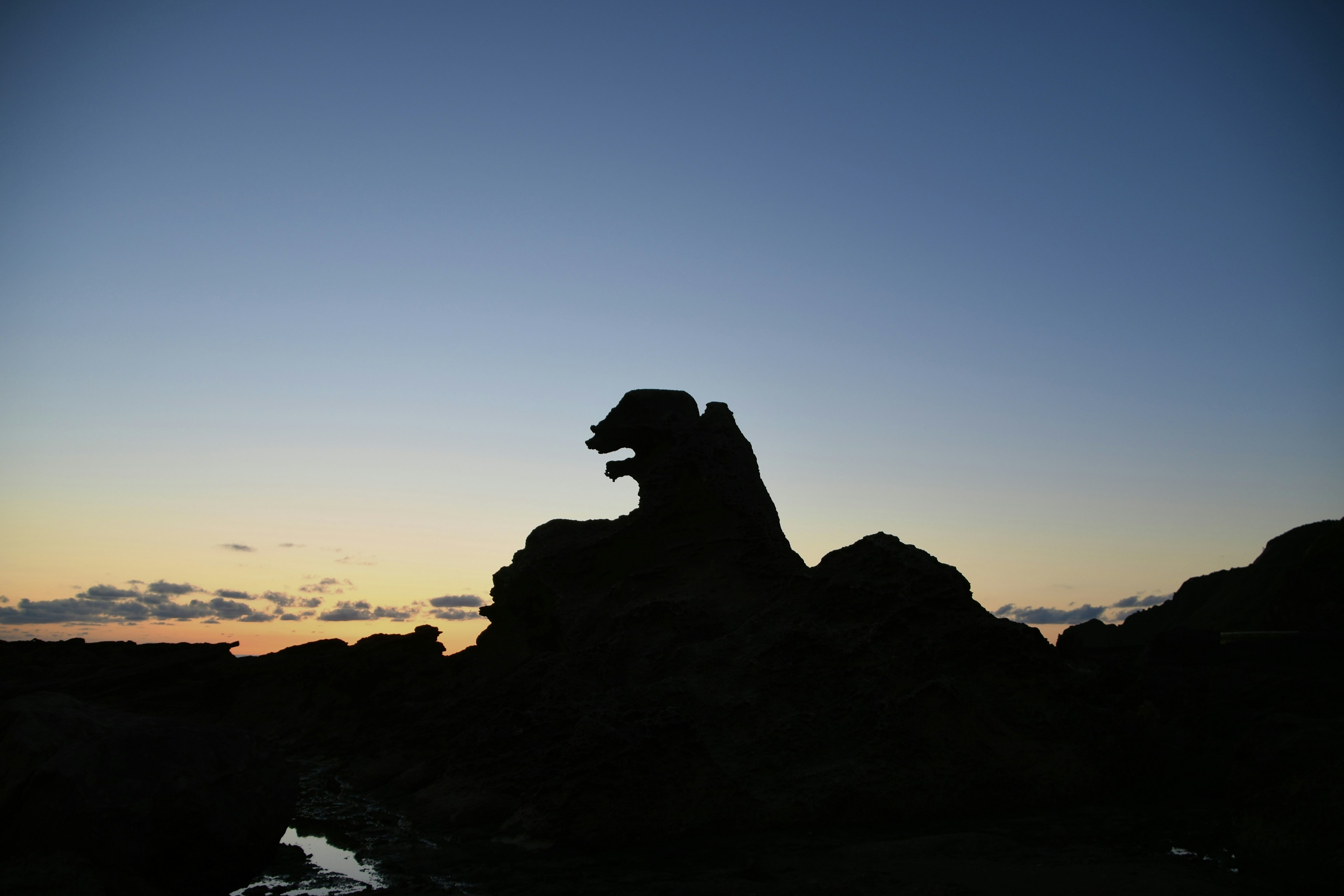 Silueta de una formación rocosa que parece un lobo contra un cielo de atardecer