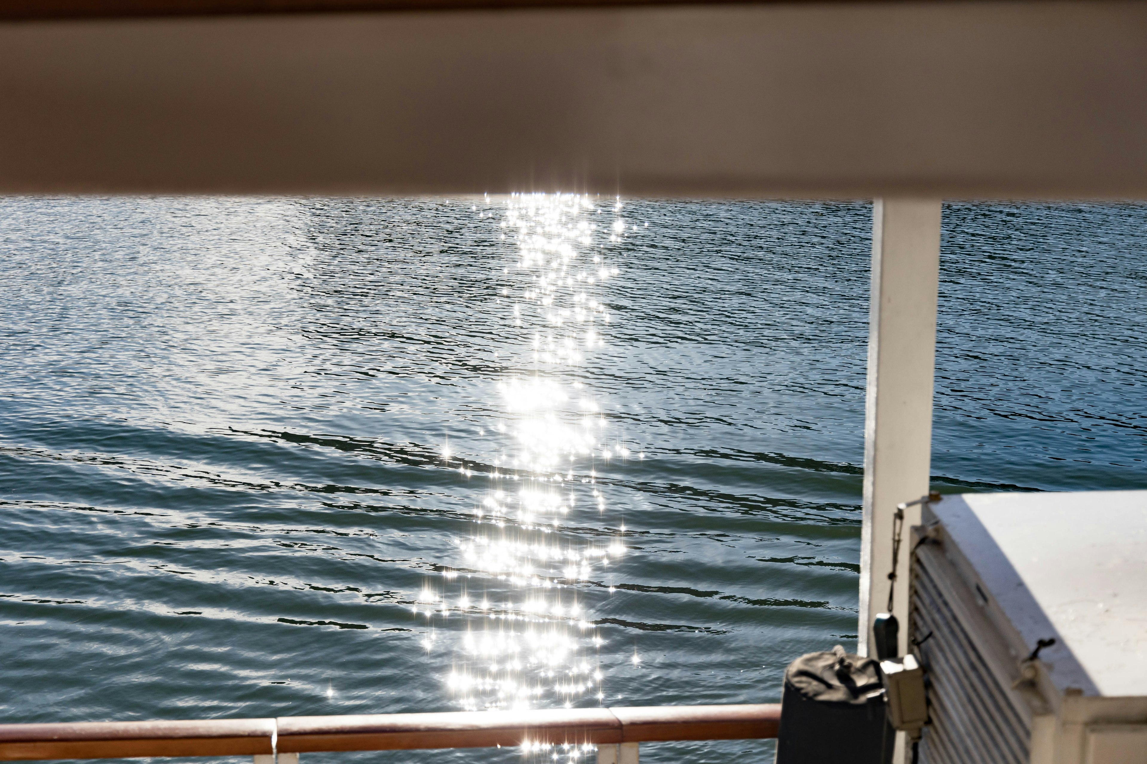 Eine Sicht auf das schimmernde Sonnenlicht, das sich auf den Wasserwellen spiegelt, mit einem Teil eines Bootes sichtbar