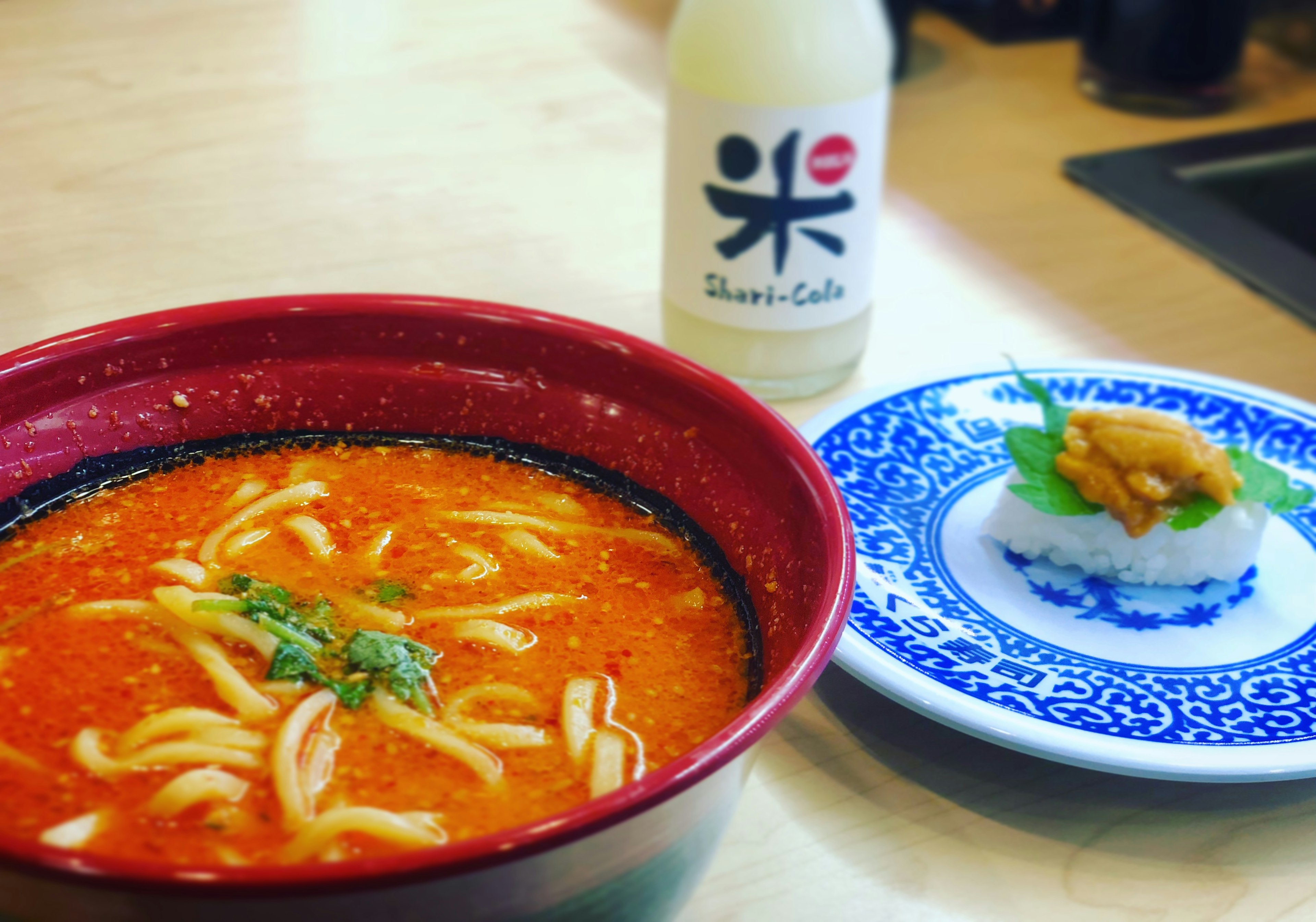 Ramen pedas di mangkuk merah dengan sushi di piring biru