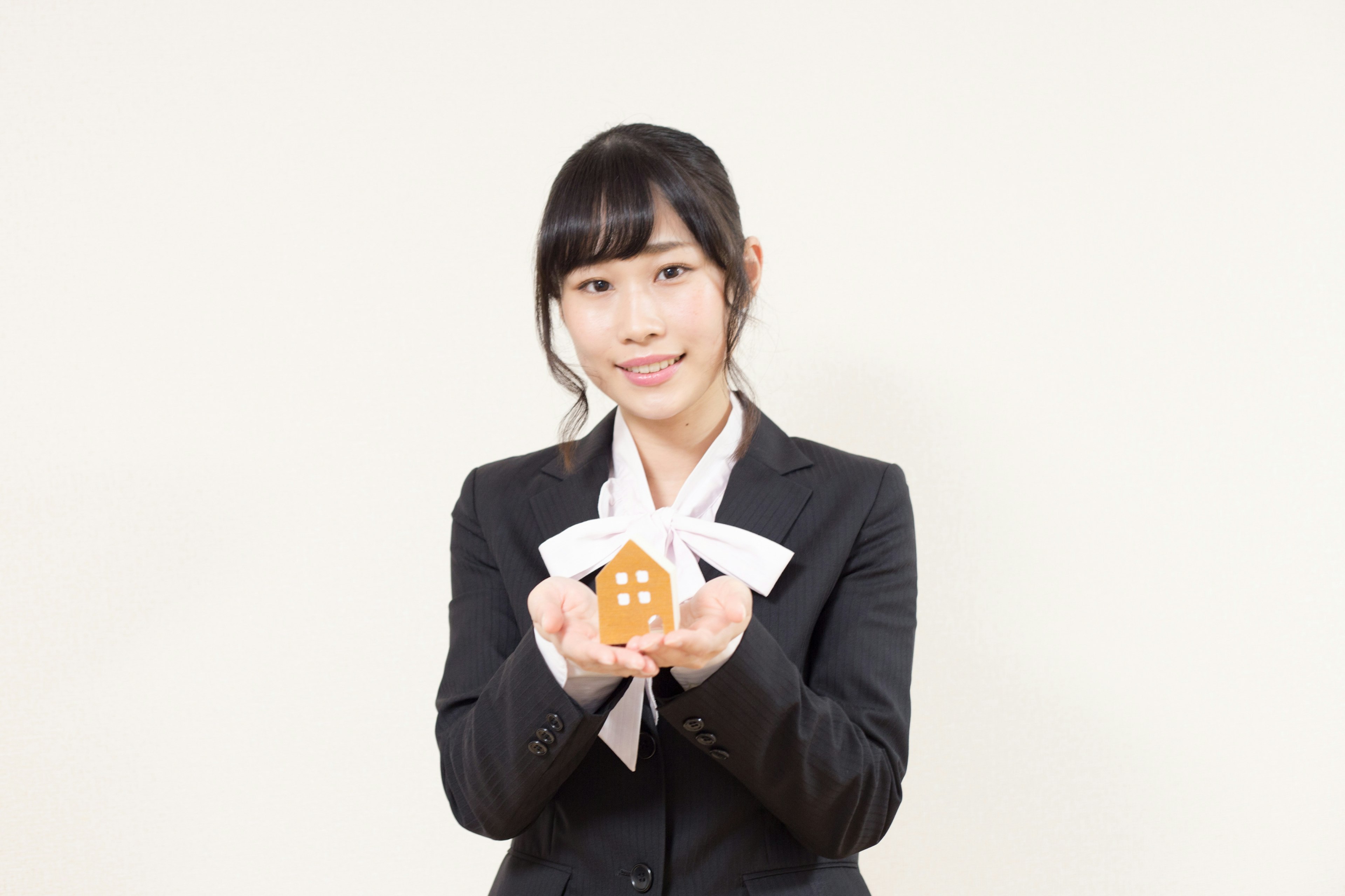 A woman in a business suit holding a small house model