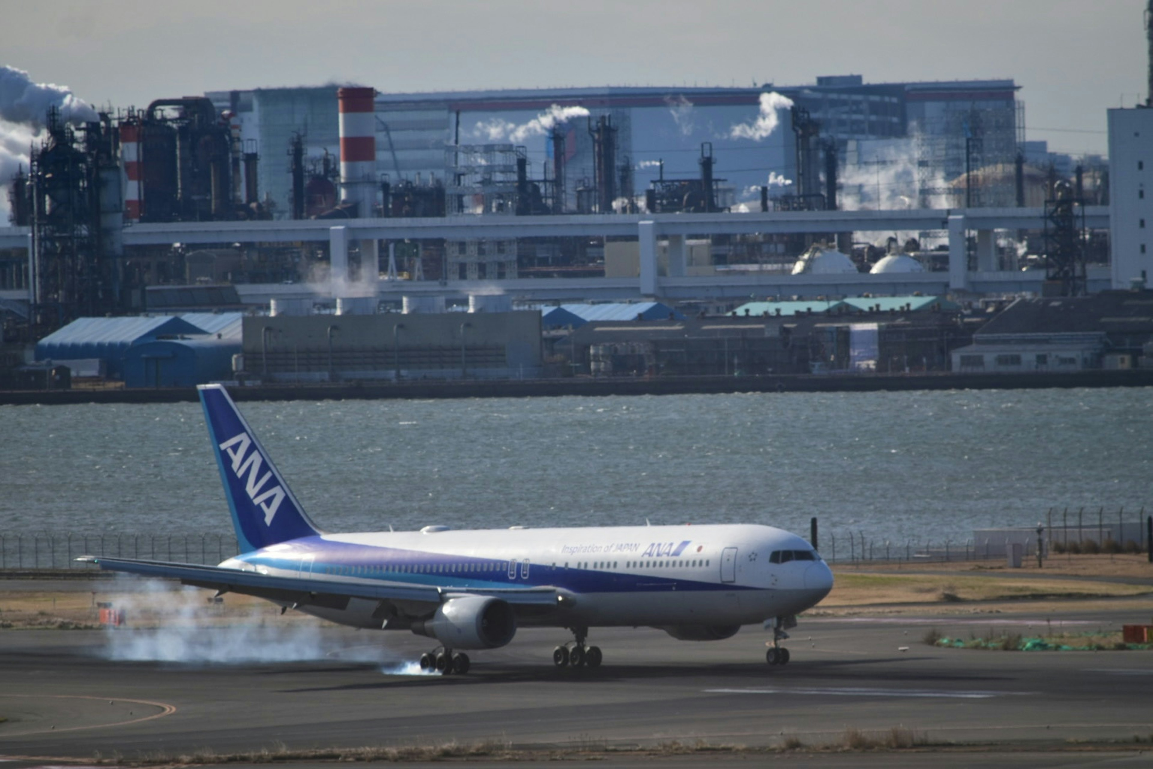 ANA airplane taxiing on runway with industrial area in background