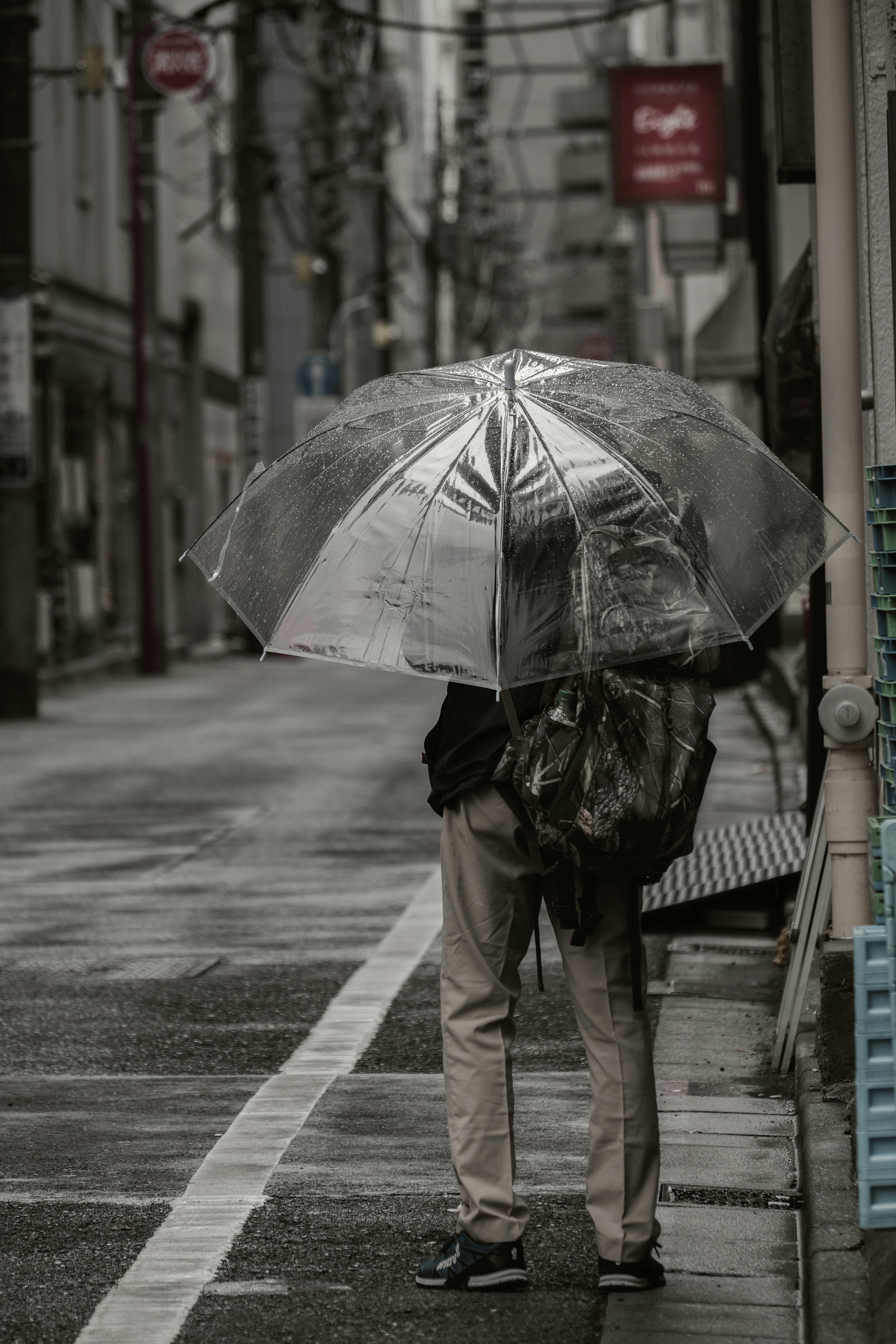 Une personne marchant sous la pluie avec un parapluie transparent dans un paysage urbain monochrome