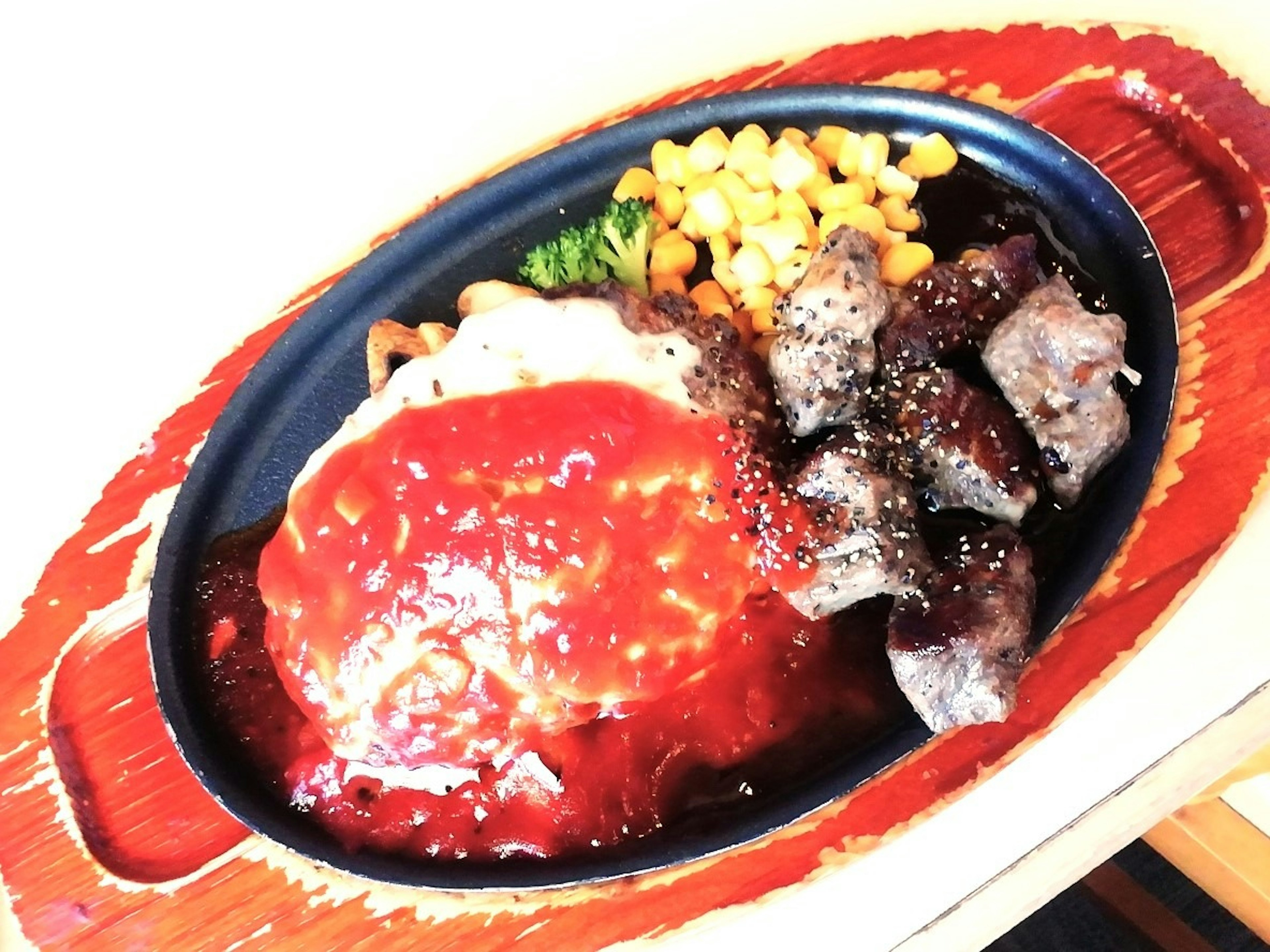 Sizzling plate with hamburger steak and sides of vegetables and corn