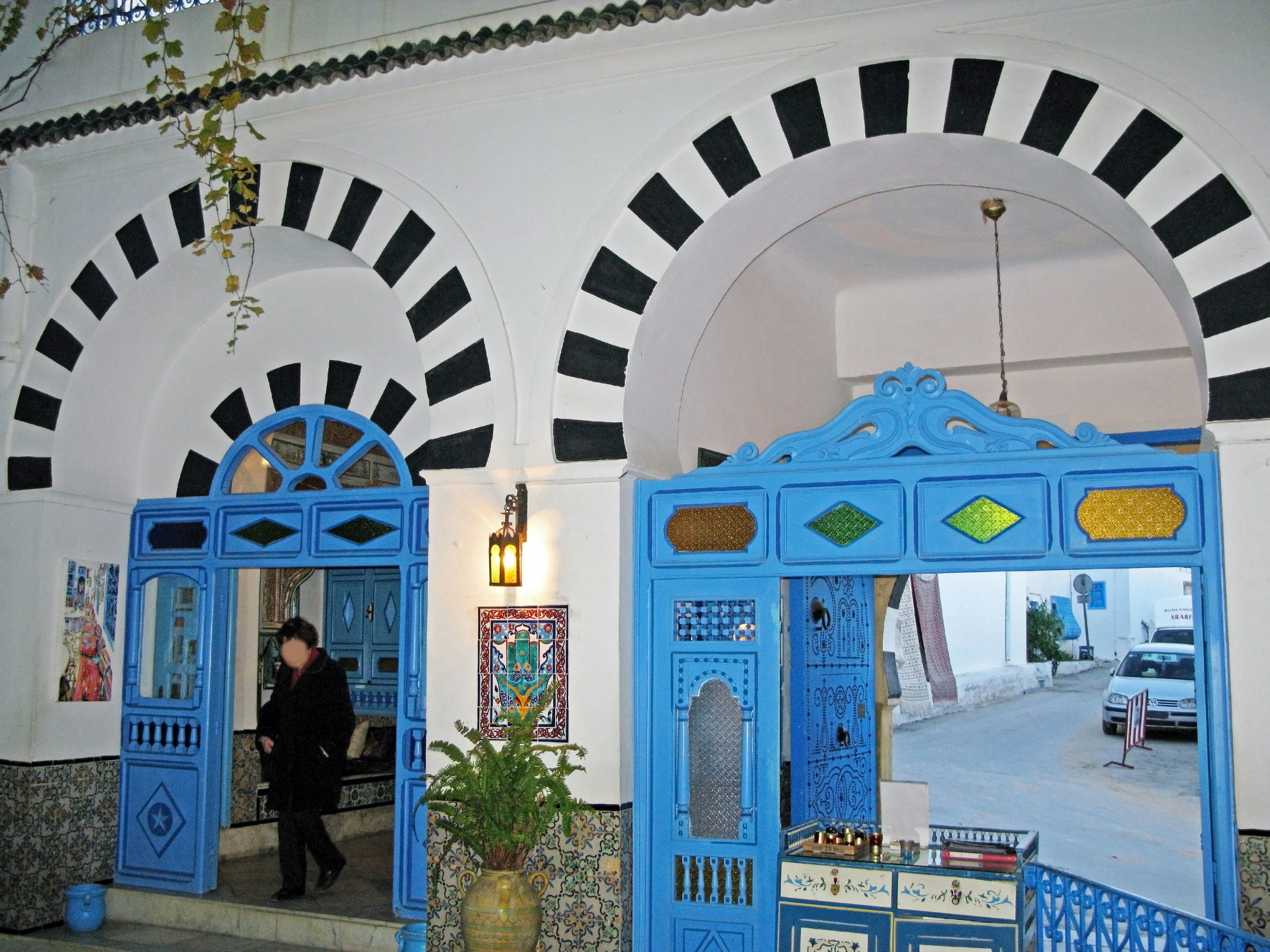 Entrance with blue doors and black and white arches featuring a person standing