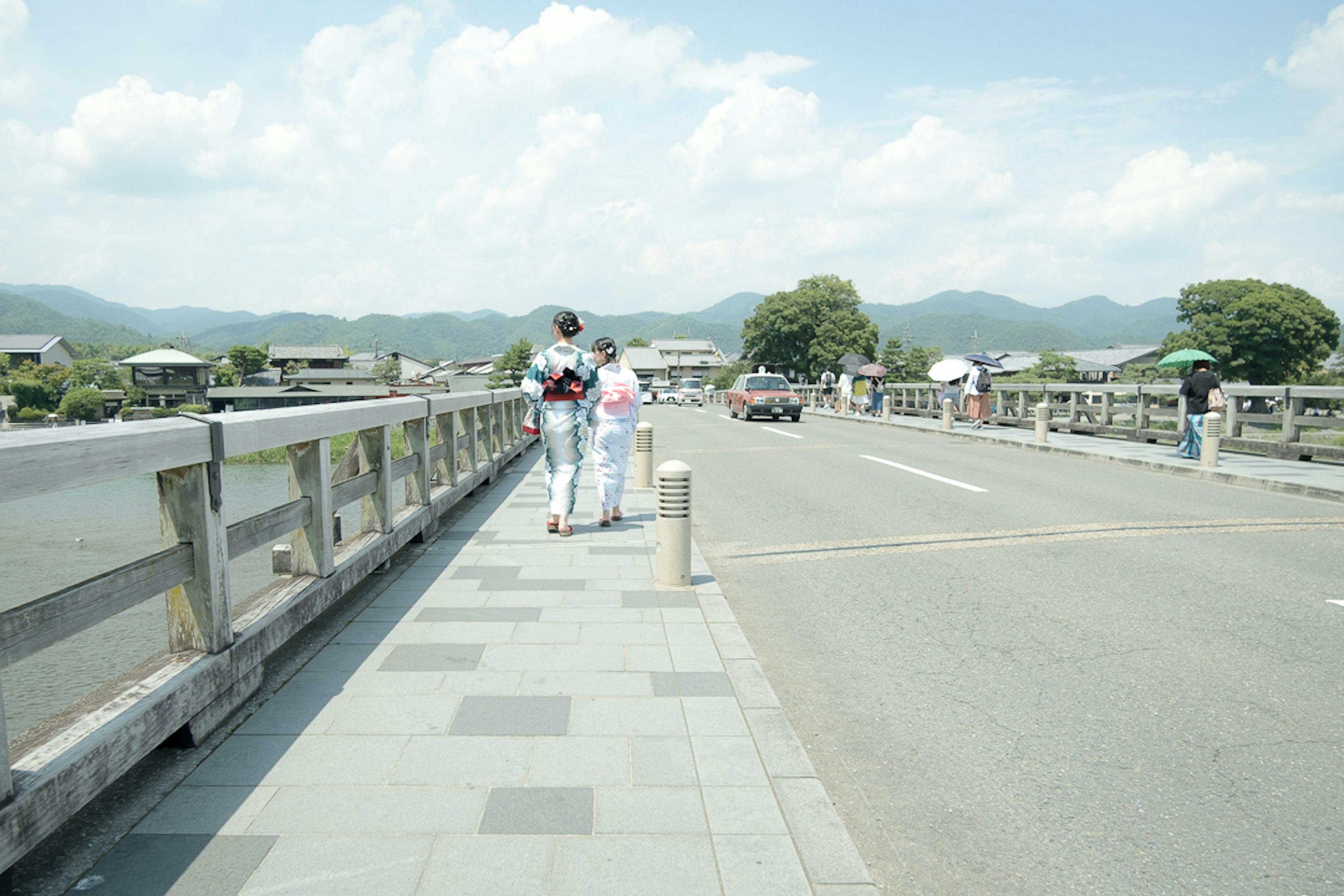 Una pareja con ropa blanca caminando sobre un puente con montañas al fondo