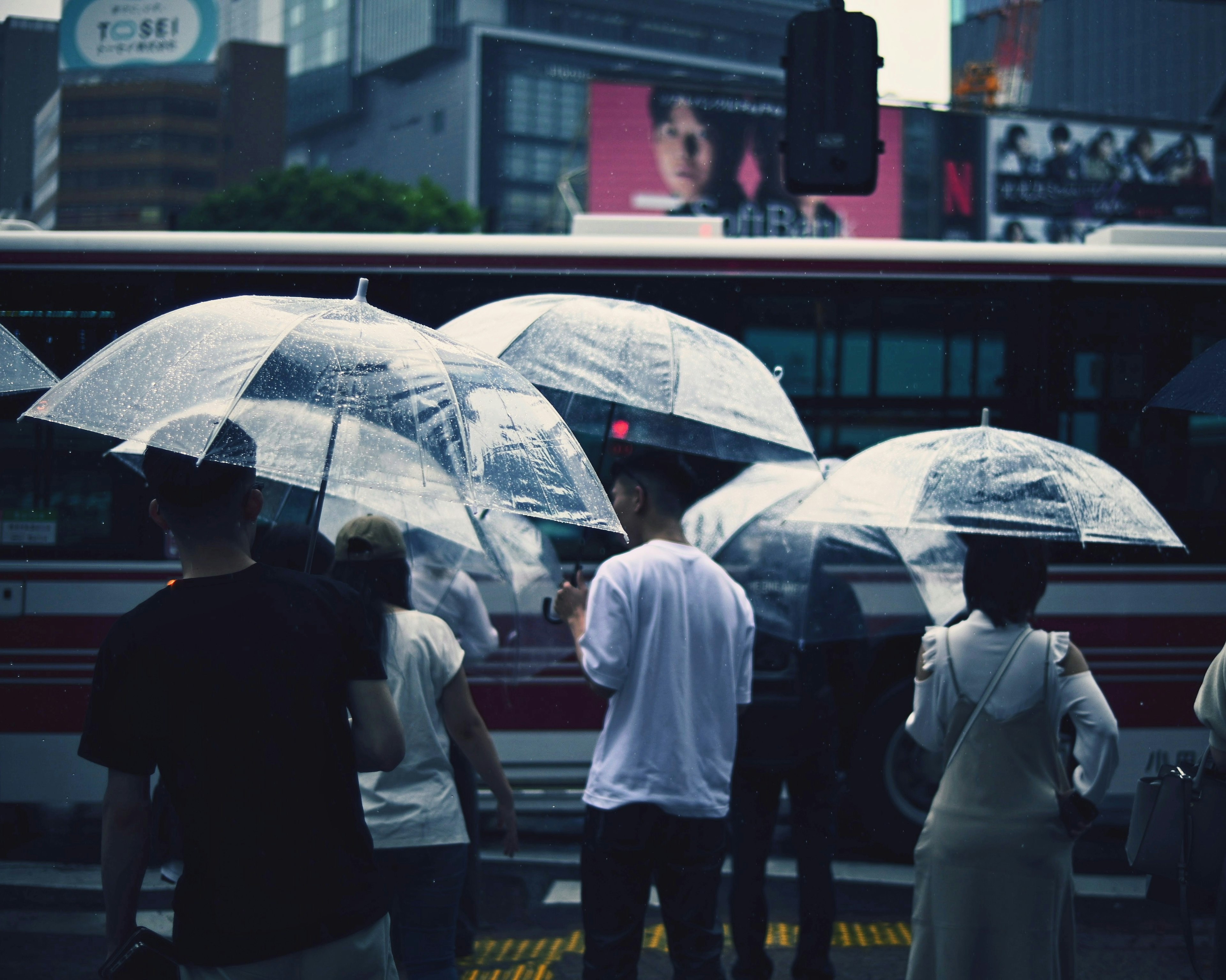 人們在雨中拿著傘站在十字路口，背景是城市風景