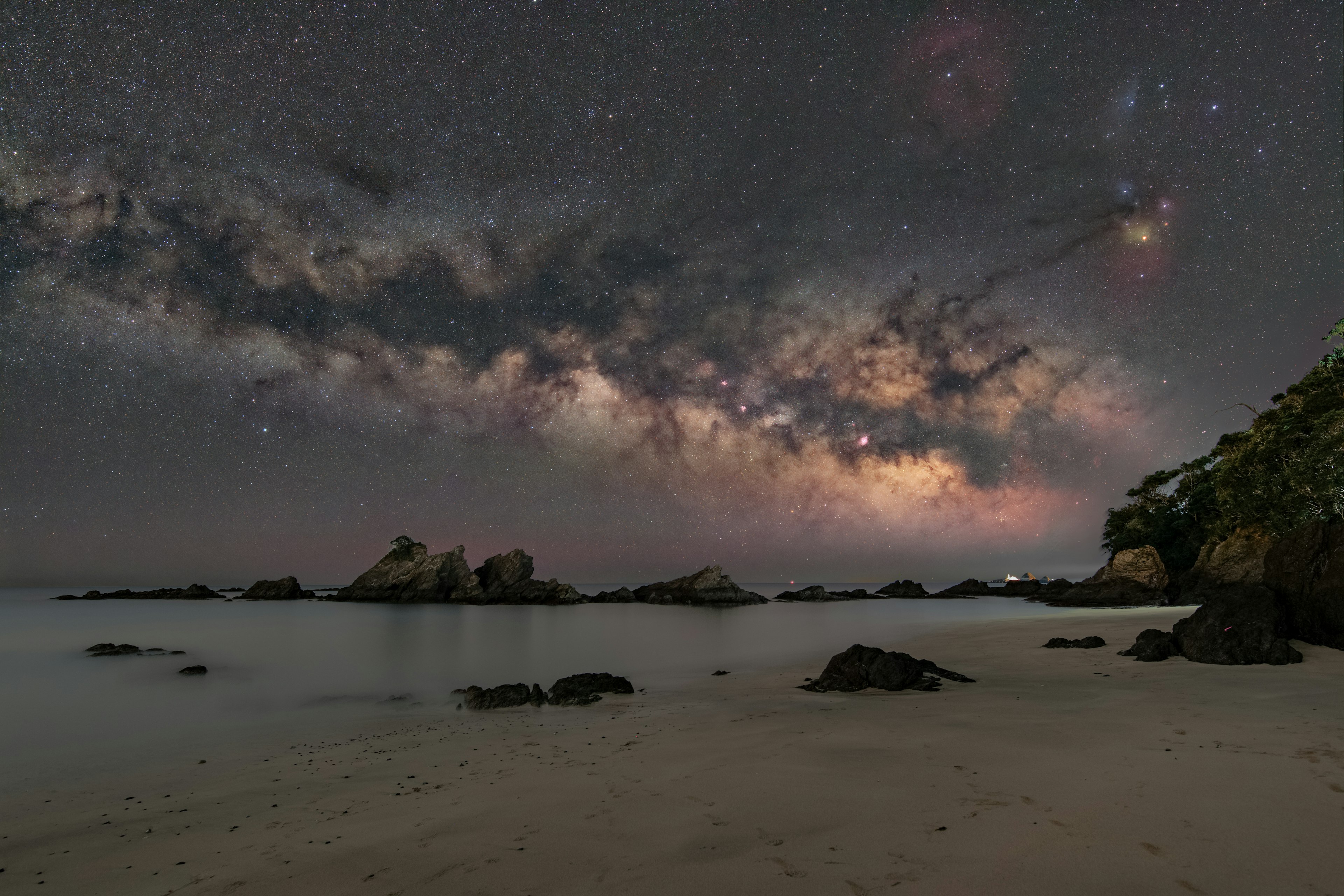 夜空に広がる天の川と海の岩が映るビーチの風景