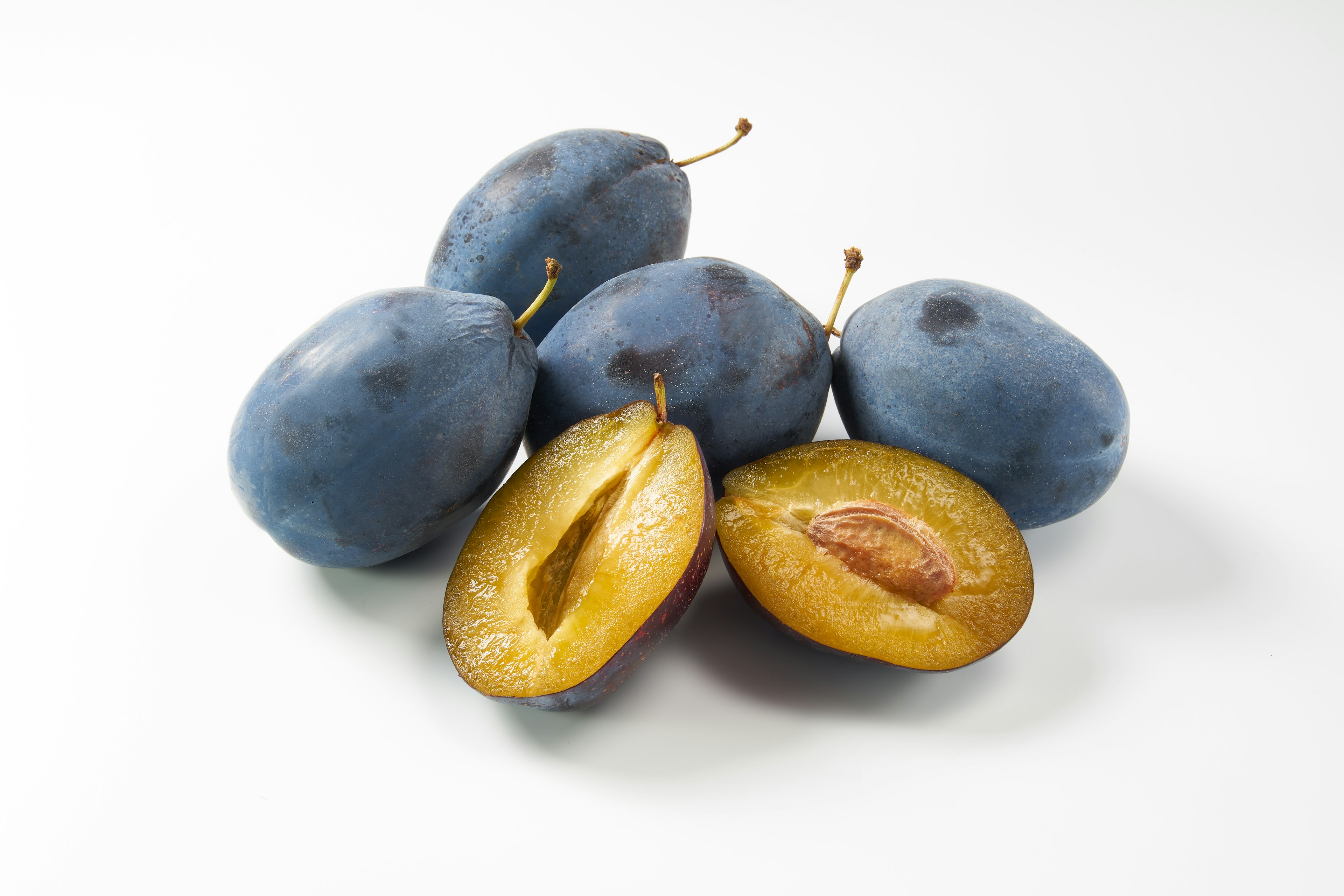 Five blue plums with one cut in half showing the yellow flesh and seed