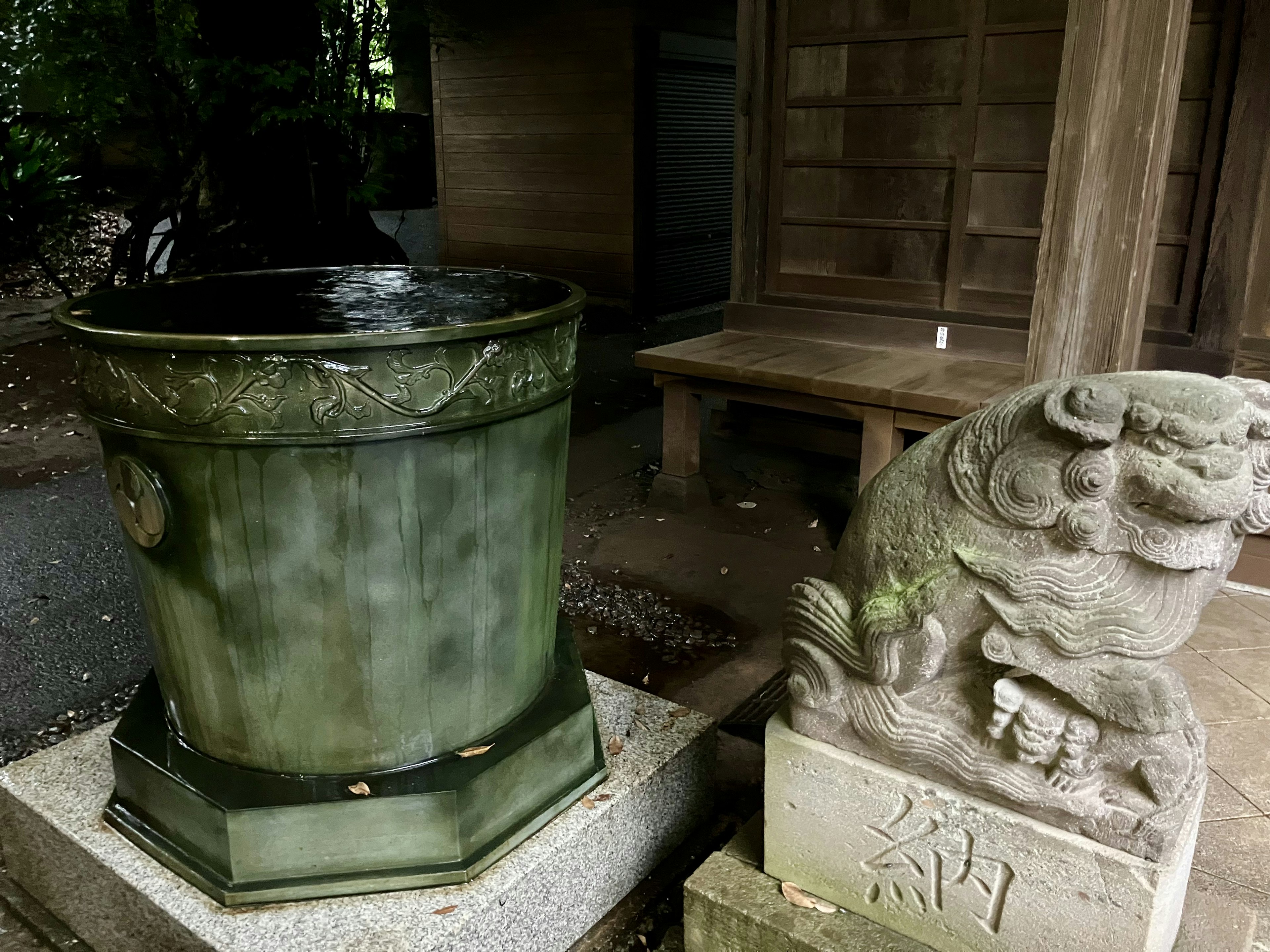 緑色の水鉢と石製の獅子像が並ぶ神社の風景