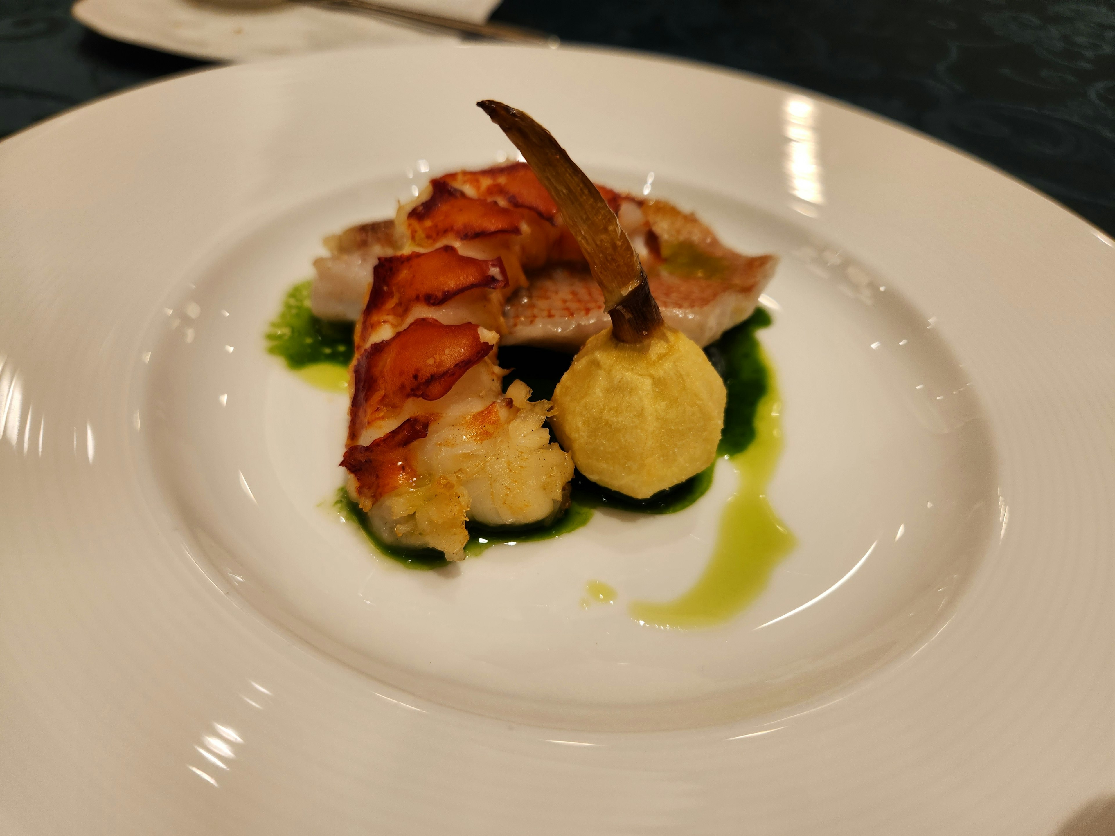 Un plat magnifiquement présenté avec du homard et une boule de purée de pommes de terre sur un lit de sauce verte