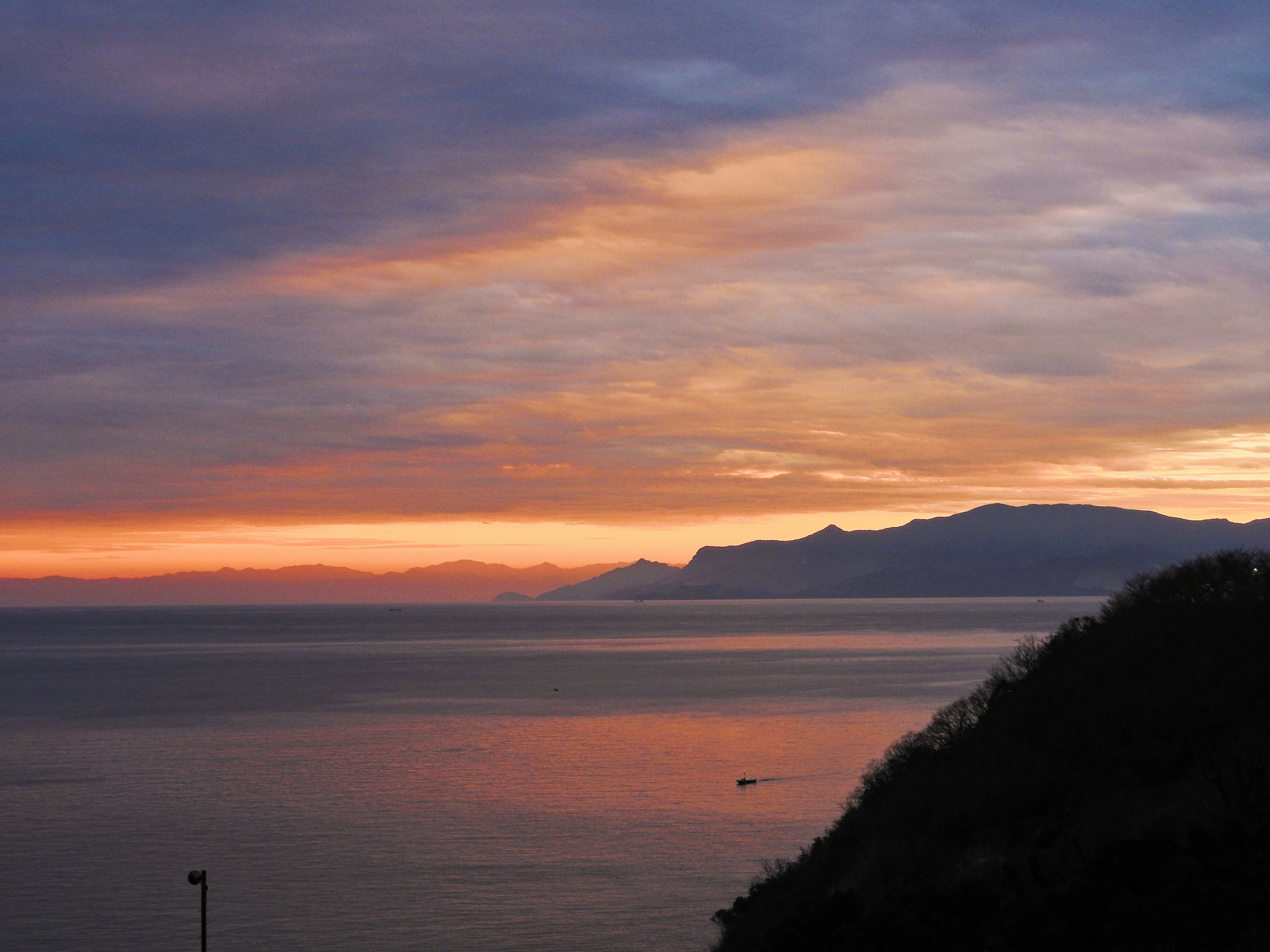 Schöner Sonnenuntergang, der sich auf dem Meer spiegelt, mit Silhouetten von Bergen