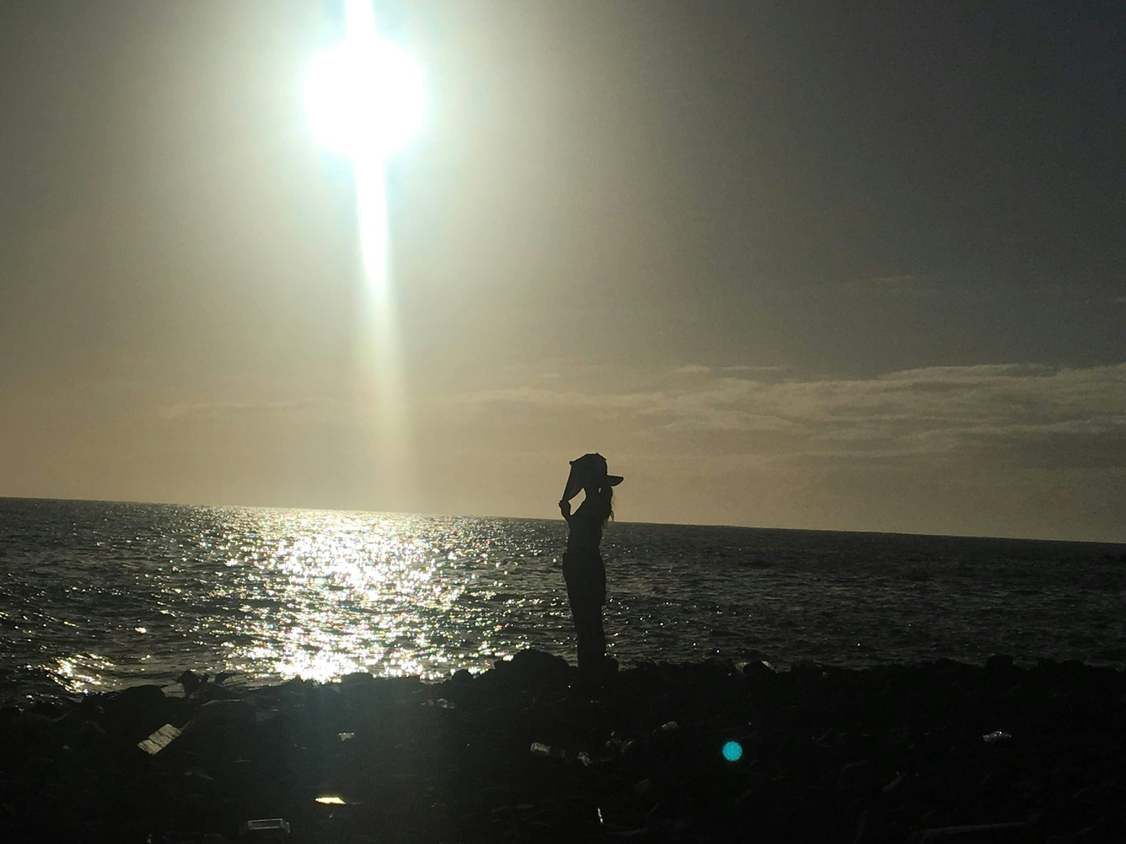 Silhouette of a person wearing a hat on the beach under bright sunlight