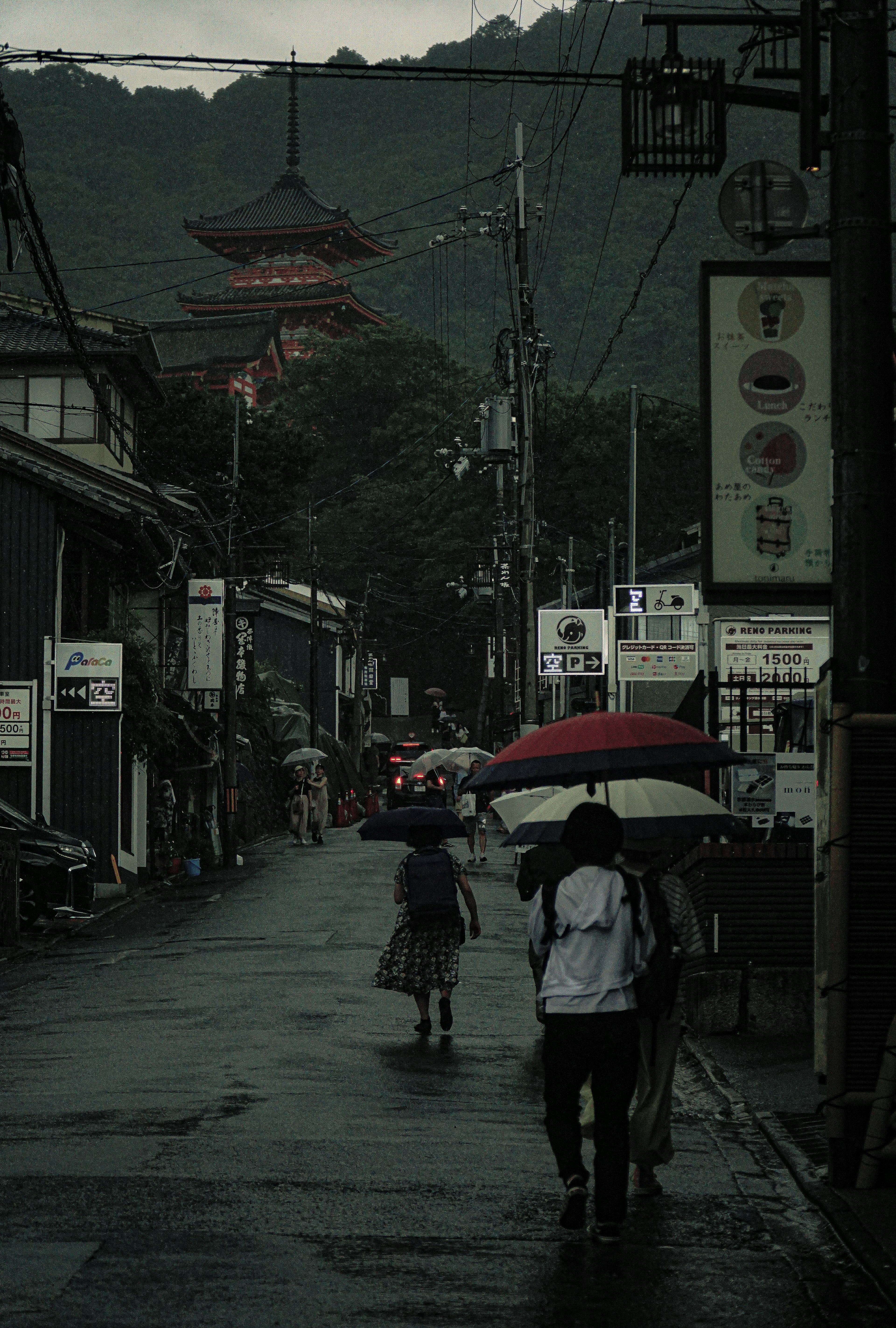 雨の中を歩く人々と背景にある赤い寺の景色