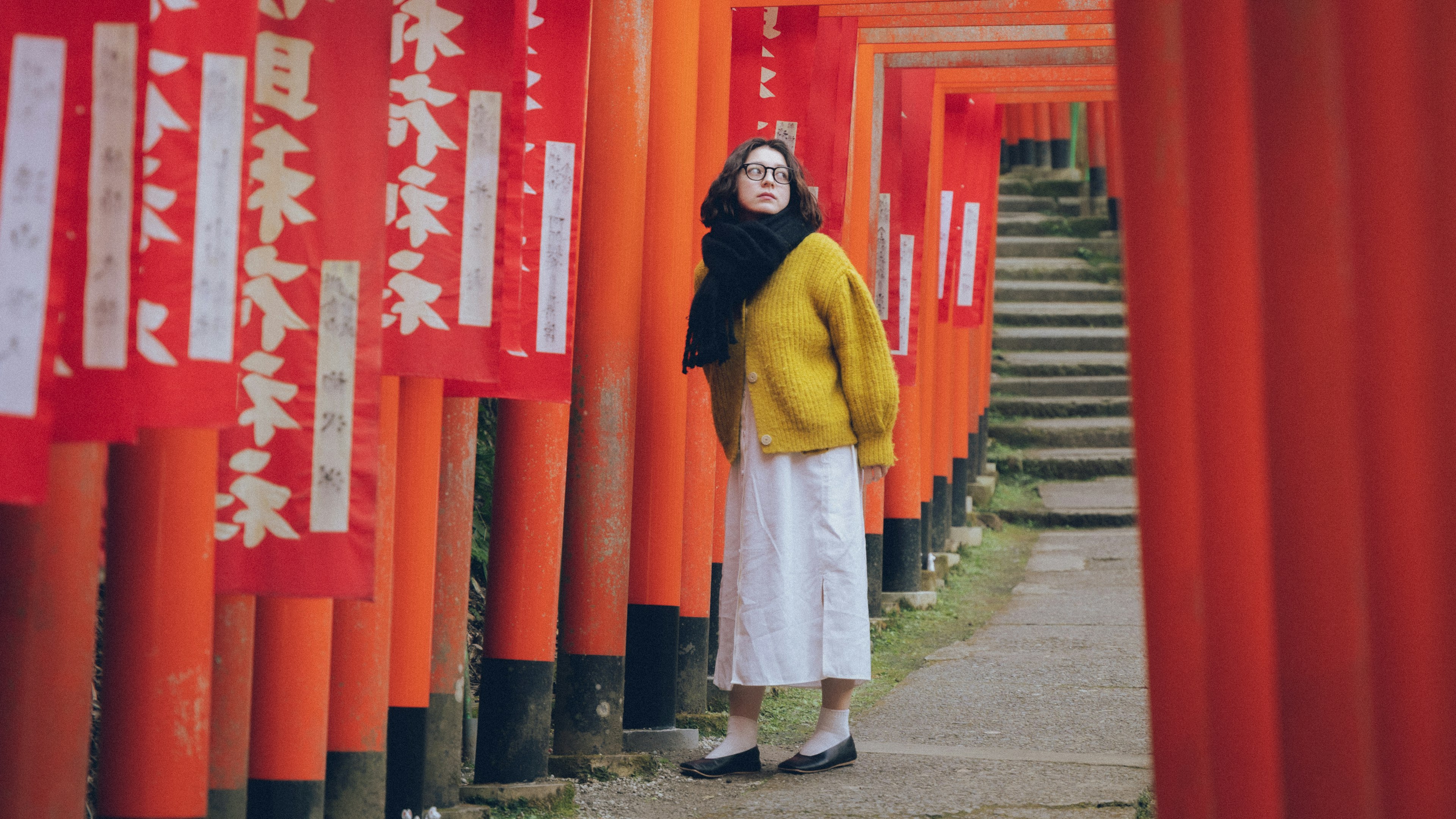 Una donna in maglione giallo in piedi tra torii rossi