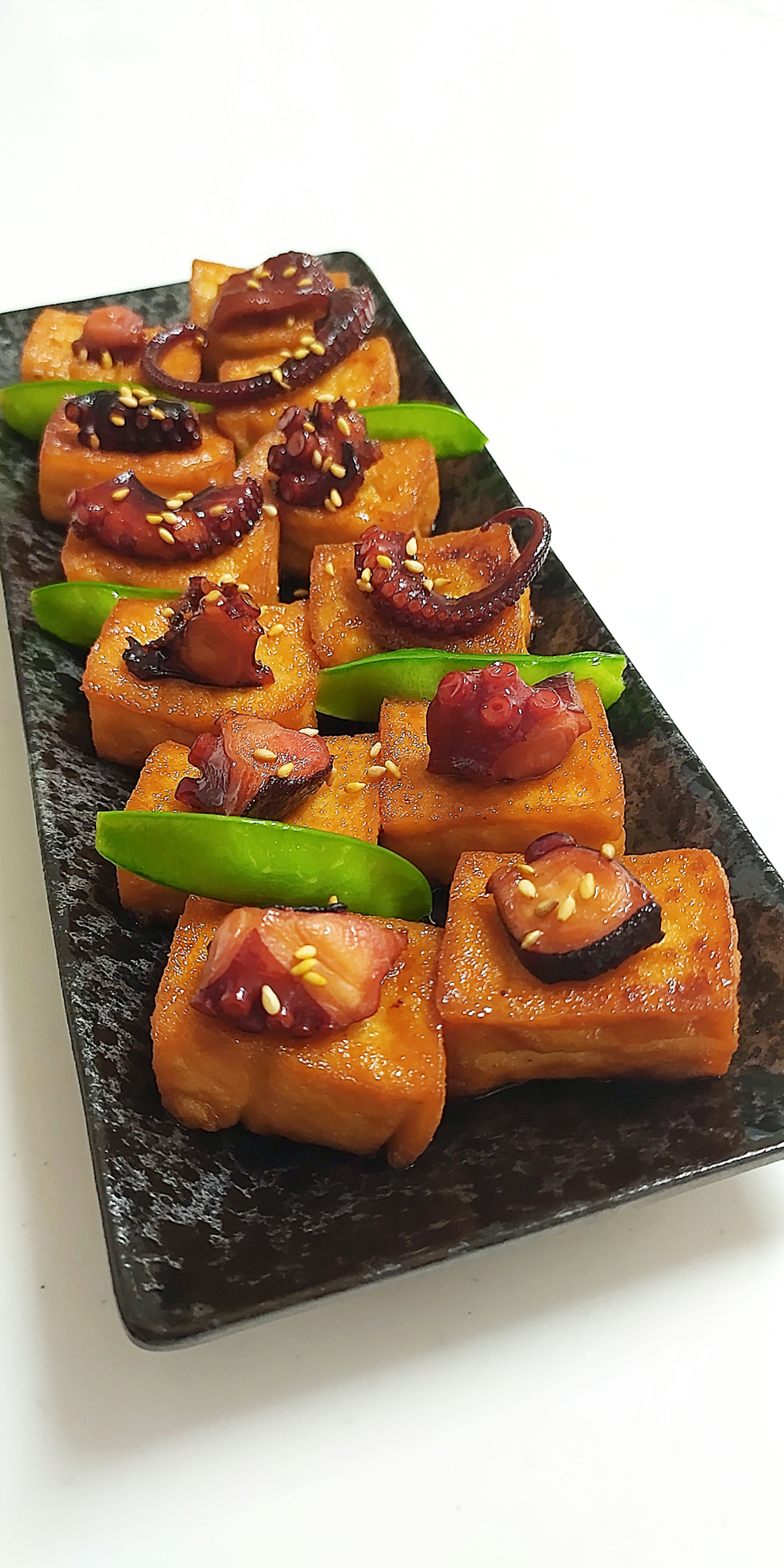 Delicious tofu dish arranged on a black plate with toppings