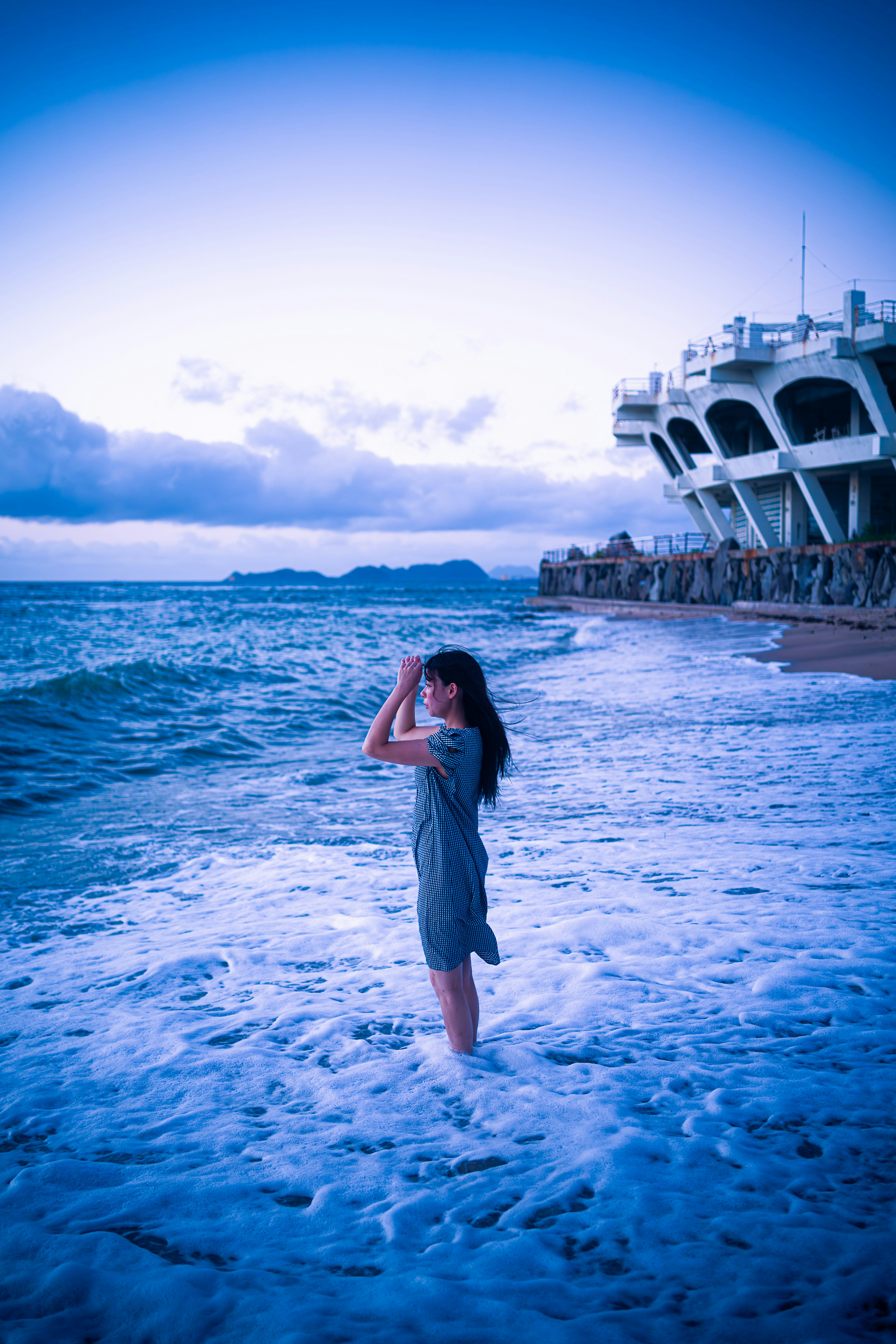 海岸で波に足を浸しながらポーズを取る女性の青いトーンの写真